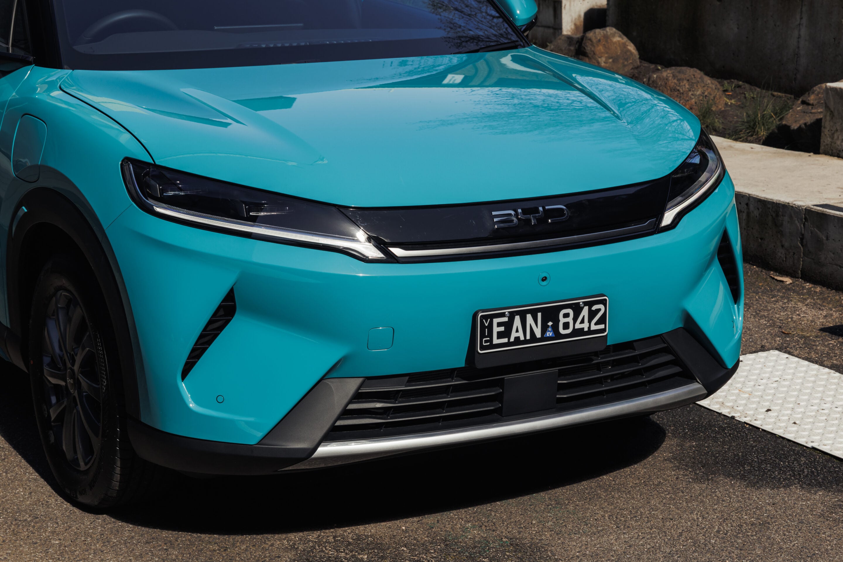 Close-up of a turquoise car's front end, showing an LED headlight, black grille badge area, and visible license plate.