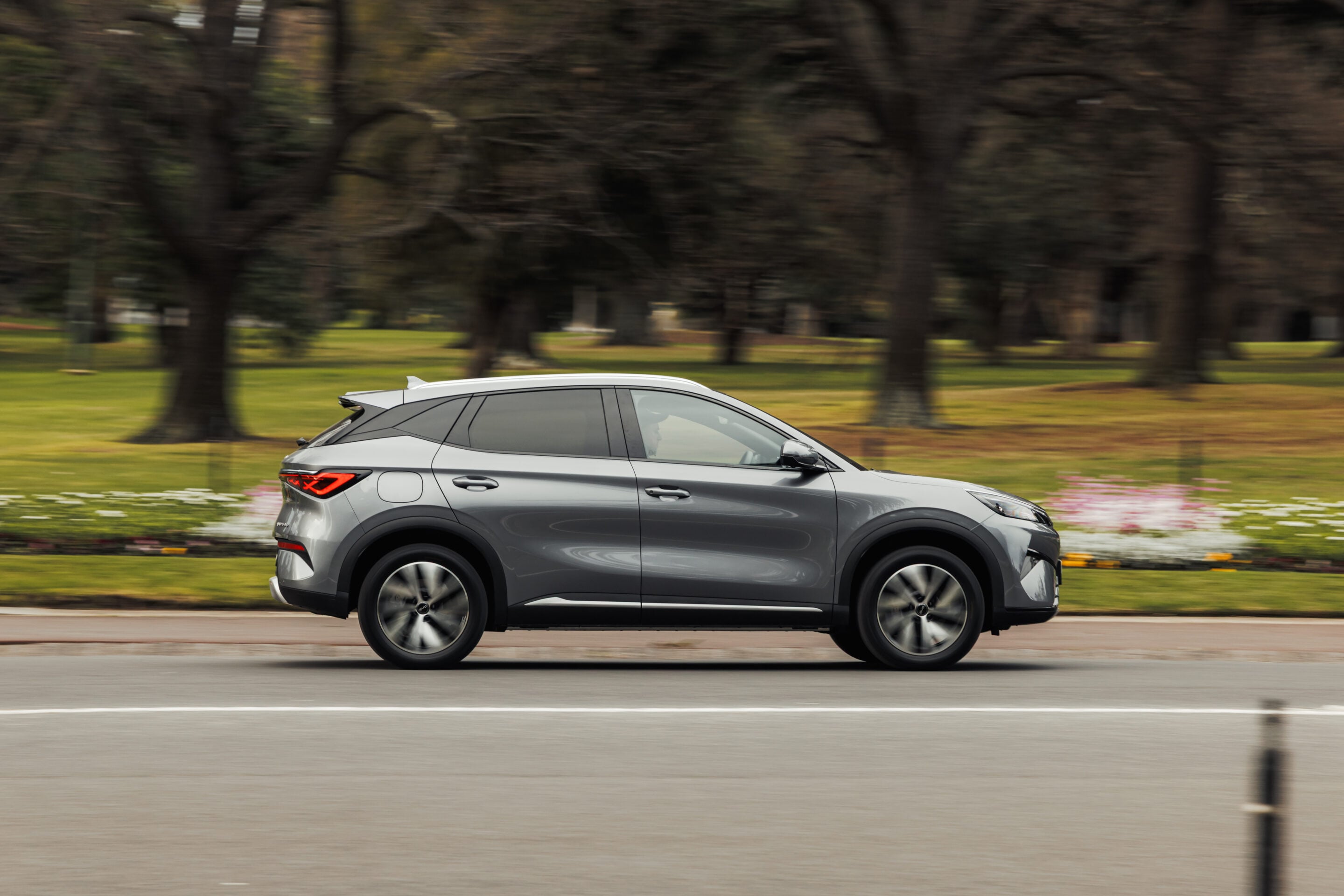 Silver SUV driving at speed along a road with a blurred park background behind it.