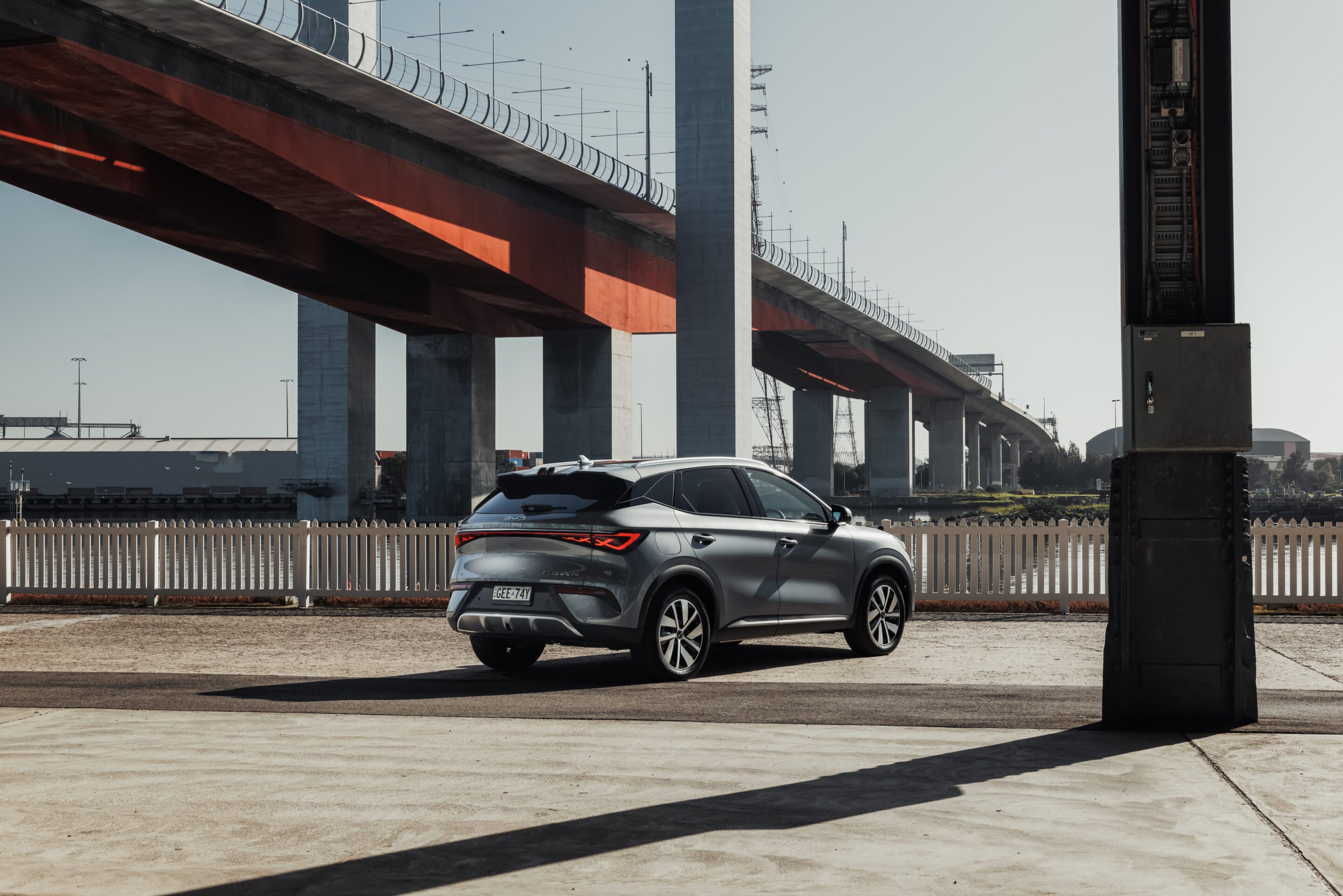 Silver SUV parked beneath a large orange-gray bridge with tall concrete pillars and railings nearby