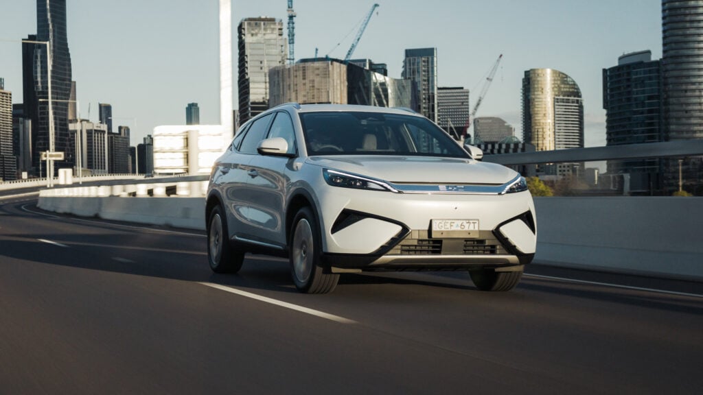 White SUV driving on an elevated city highway with tall modern buildings in the background