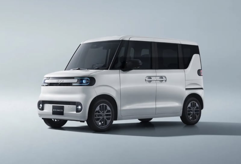 White compact minivan with black-tinted windows in a studio setting, showing sliding doors and a rounded front end.