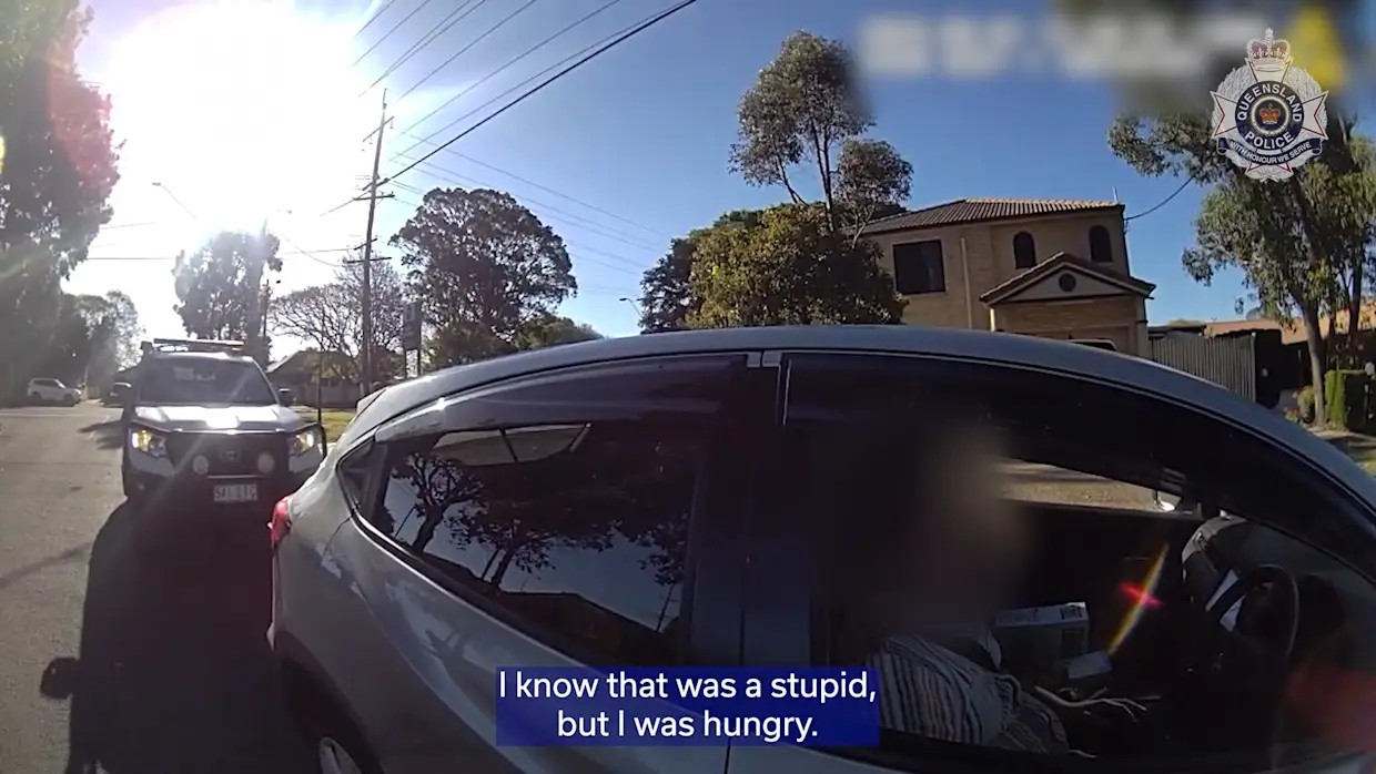 Dashcam POV of a white SUV being followed by a police vehicle on a residential street, with a house and trees in the background and a subtitle reading, 'I know that was a stupid, but I was hungry.'