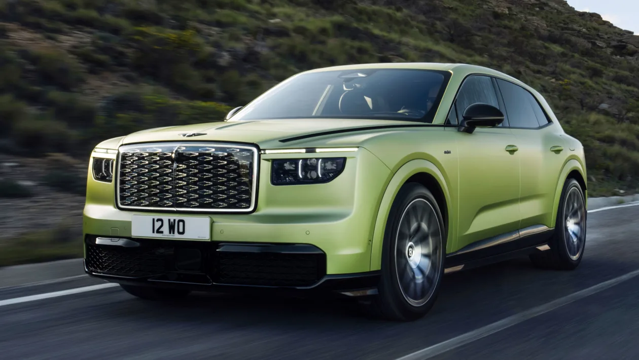 Green Bentley SUV driving on a winding road with hills in the background (front three-quarter view).
