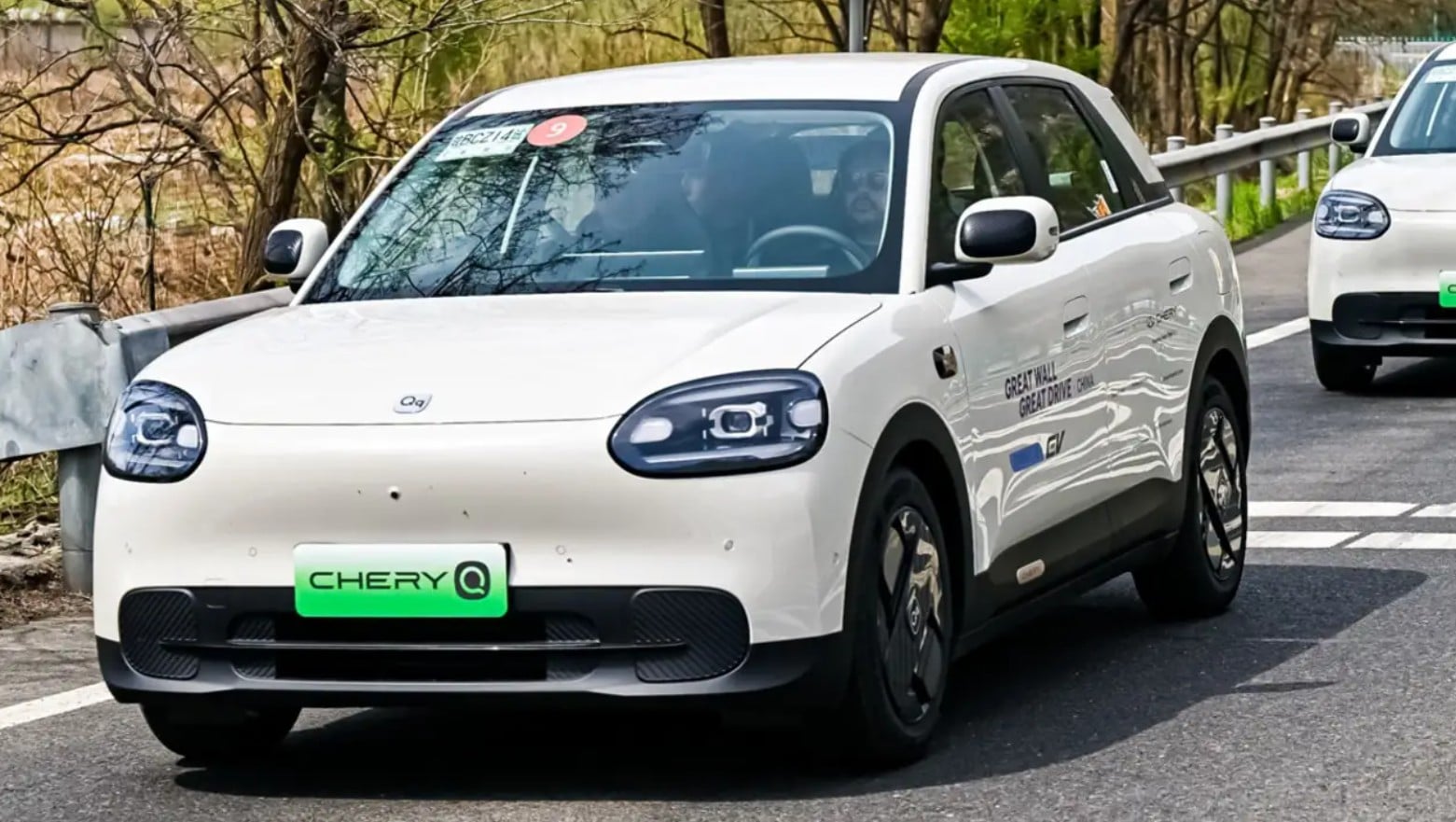 Front-left view of a white electric taxi (Chery Q) on a road, green license plate reading CHERY Q visible.