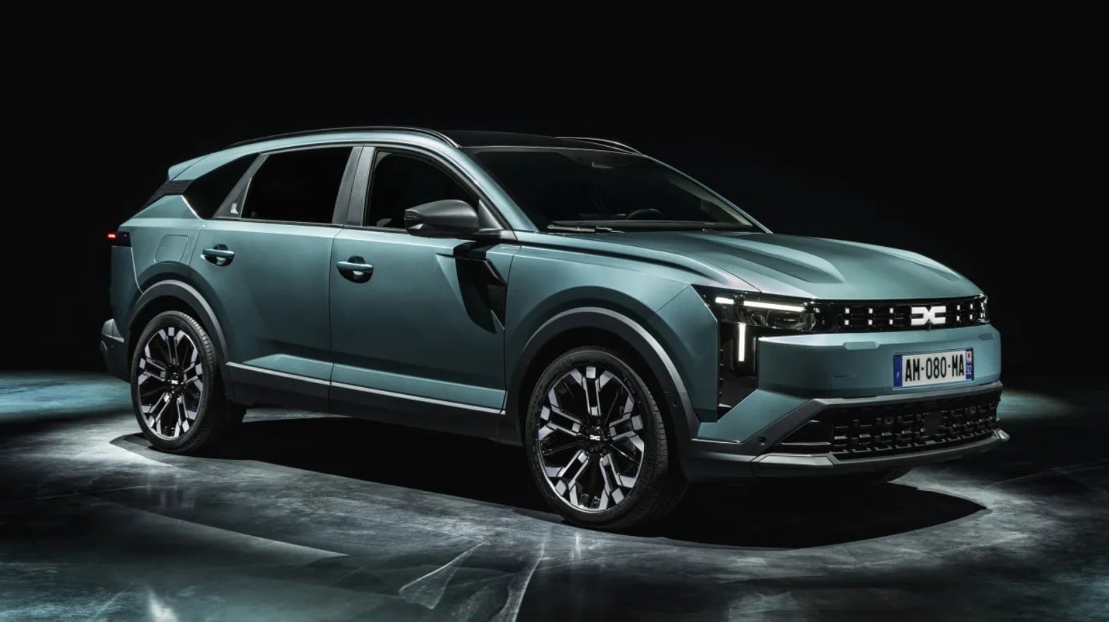 Teal SUV shown in a studio, three-quarter front view highlighting the grille and large alloy wheels on a dark backdrop, high contrast lighting