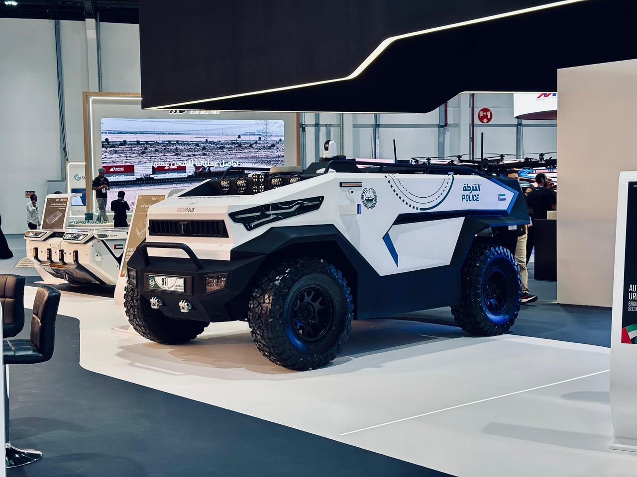 White and blue police armored vehicle on display at a technology expo or showroom set-up.