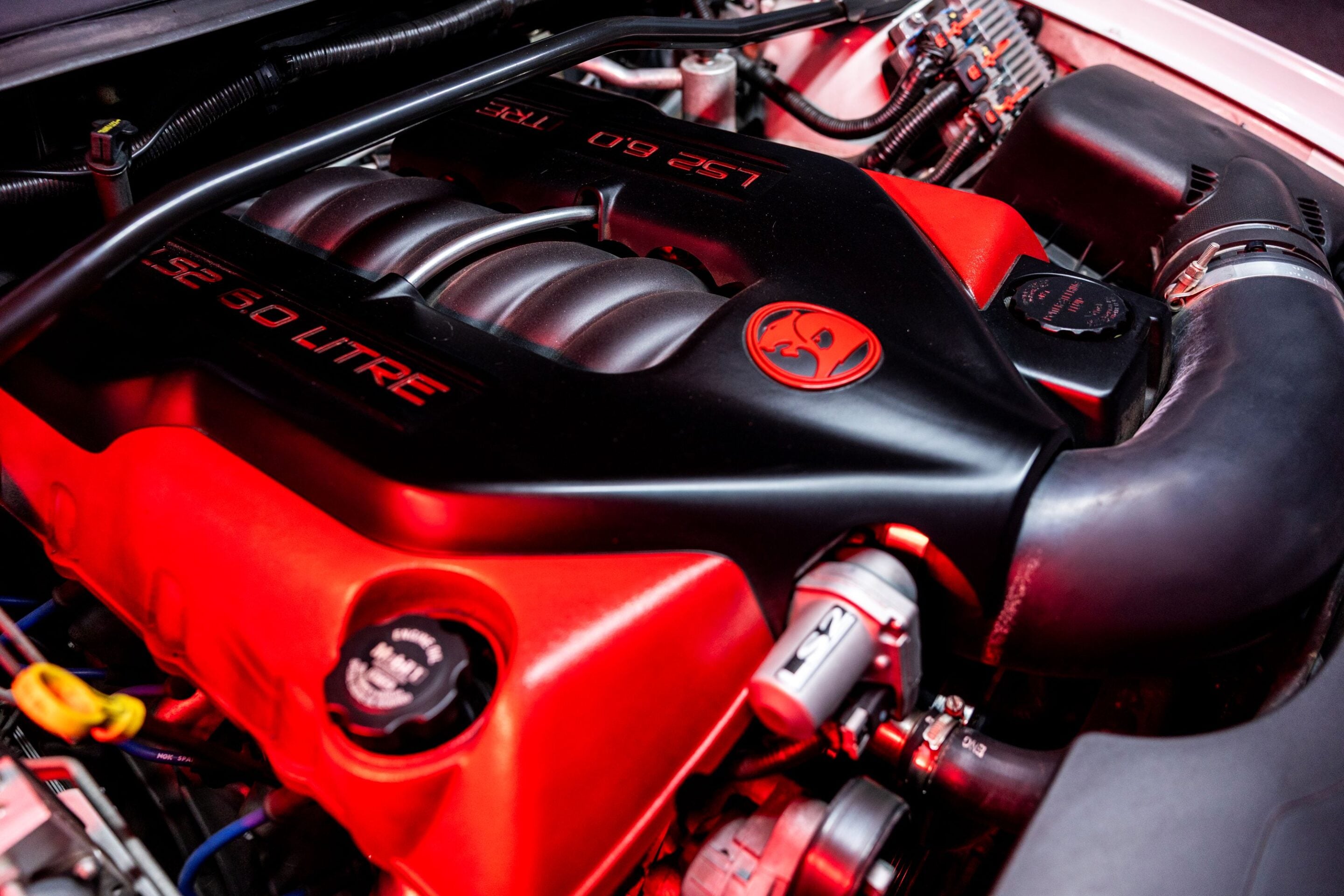 Close-up of a red and black car engine with a 6.0 LITRE label on the cover.