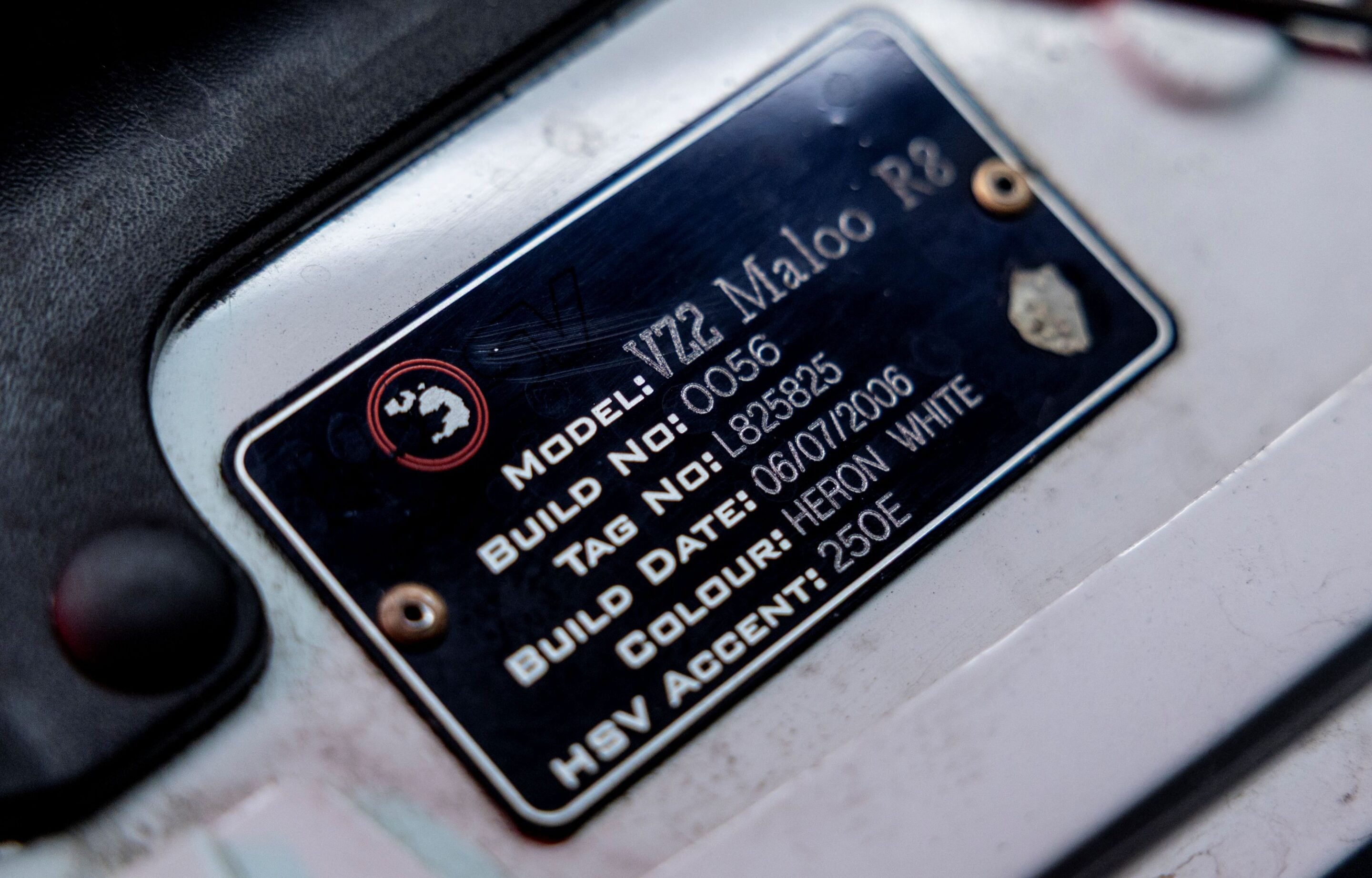 Close-up of a metal vehicle build/ID plate attached to a light surface, showing model and serial numbers.