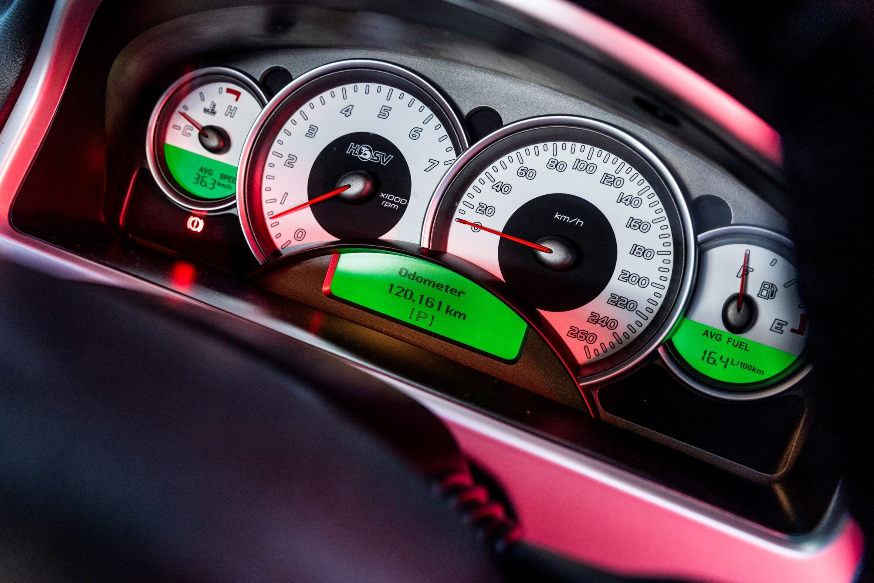 Close-up of a car instrument cluster with a large speedometer, a tachometer, and a fuel gauge; digital odometer shows 120,161 km and the display is green/red-illuminated.