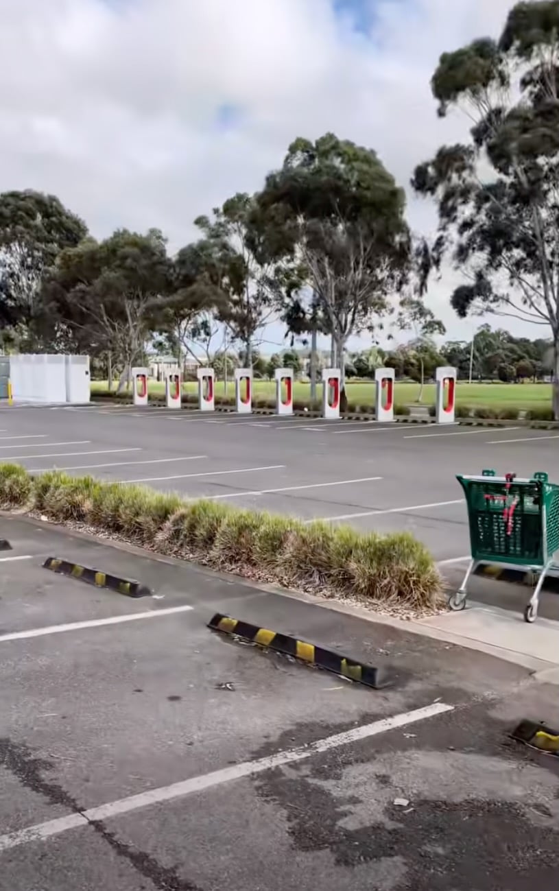Empty parking lot with a row of electric vehicle charging stations and green trees in the background.