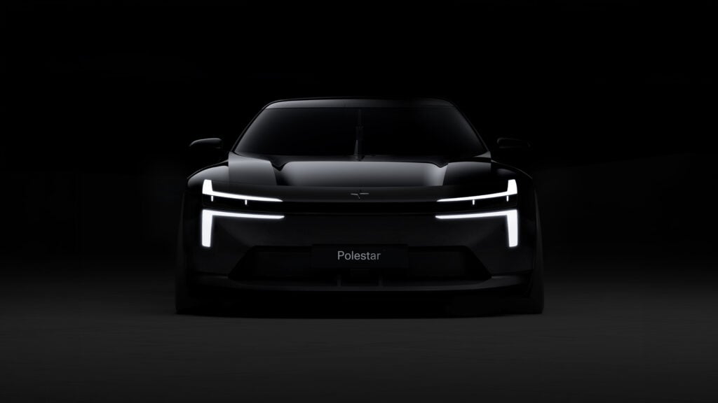 Front view of a black Polestar car illuminated by bright vertical LED headlights in a dark studio setting.