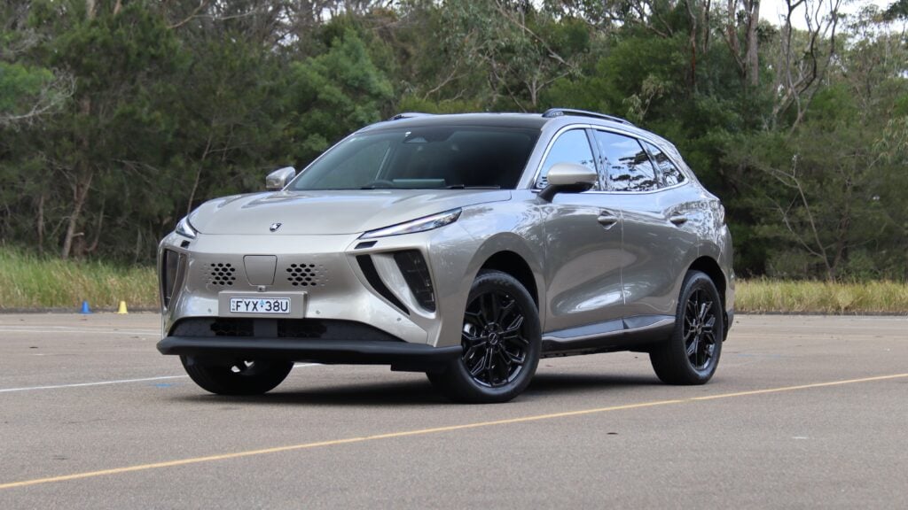 Front three-quarter view of a silver SUV parked in an empty lot with trees behind it.
