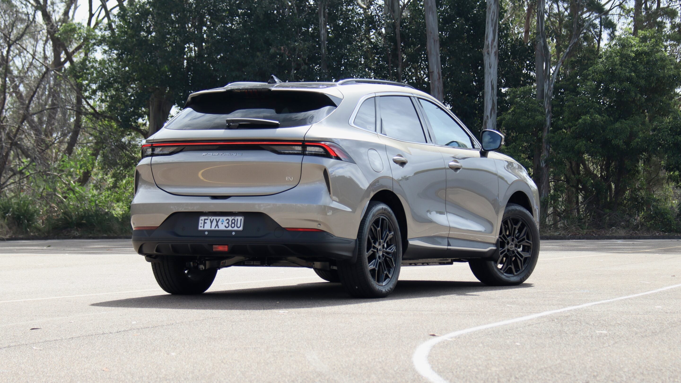 Rear three-quarter view of a silver electric SUV parked in a lot with trees in the background.