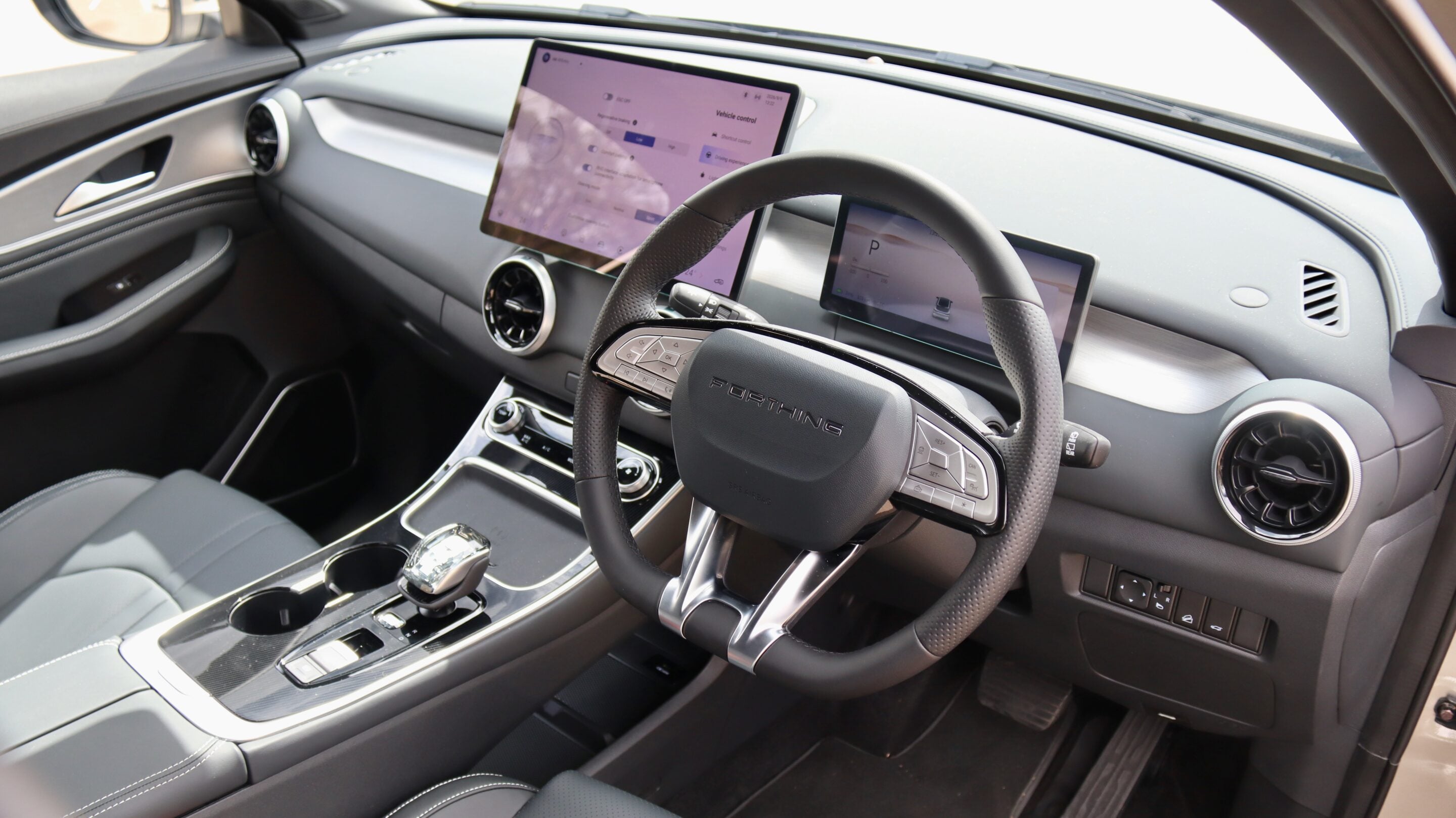 Modern car interior with a large tablet-style center screen, digital dashboard, and sporty steering wheel.