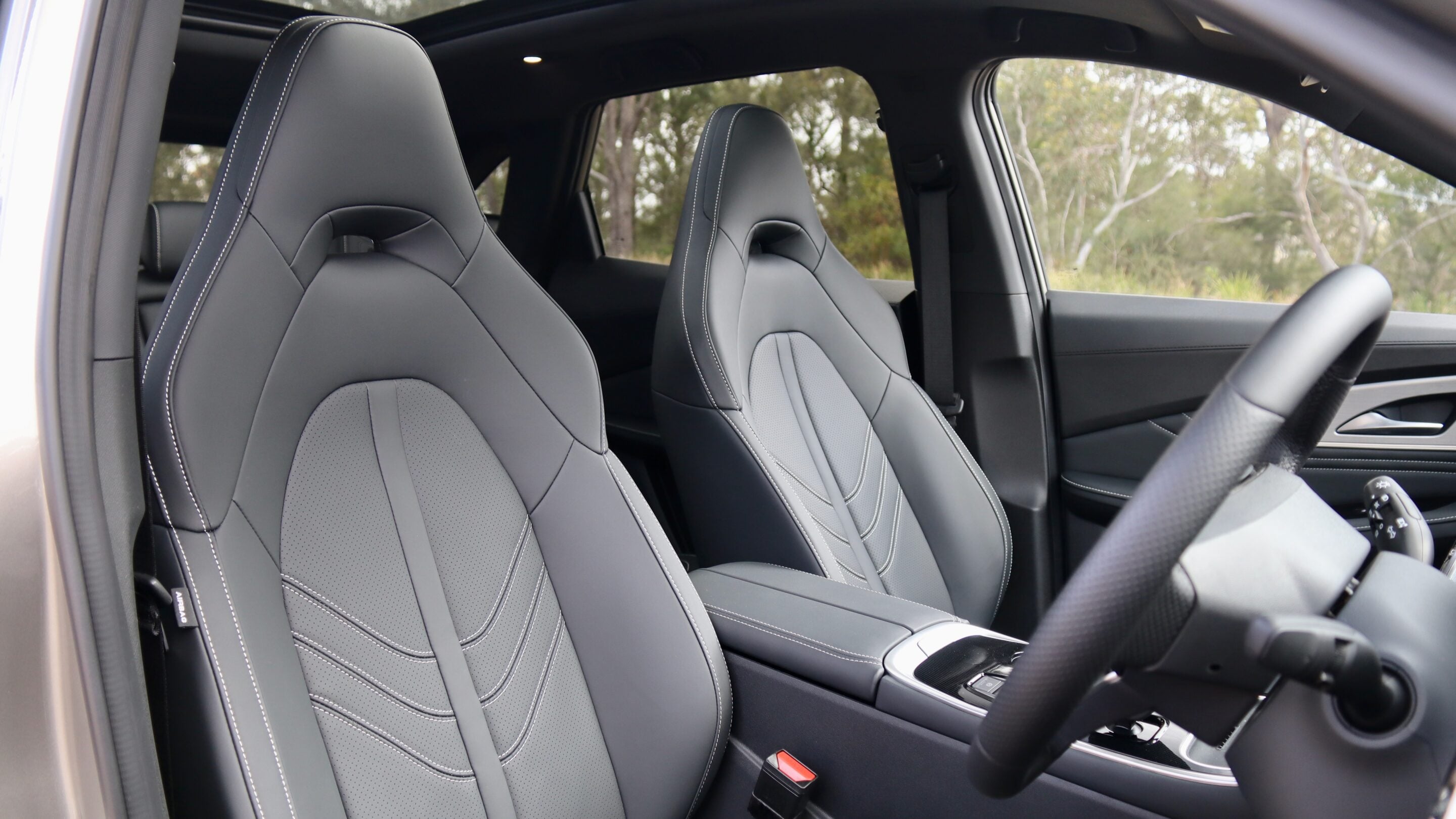 Front car seats in gray leather with white contrast stitching, visible steering wheel and center console in a modern vehicle interior.