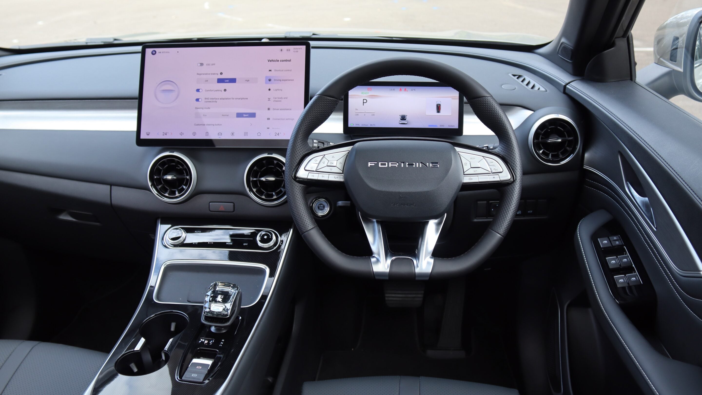 Luxury car interior with a large left touchscreen and a smaller driver display behind the steering wheel, flanked by round air vents.
