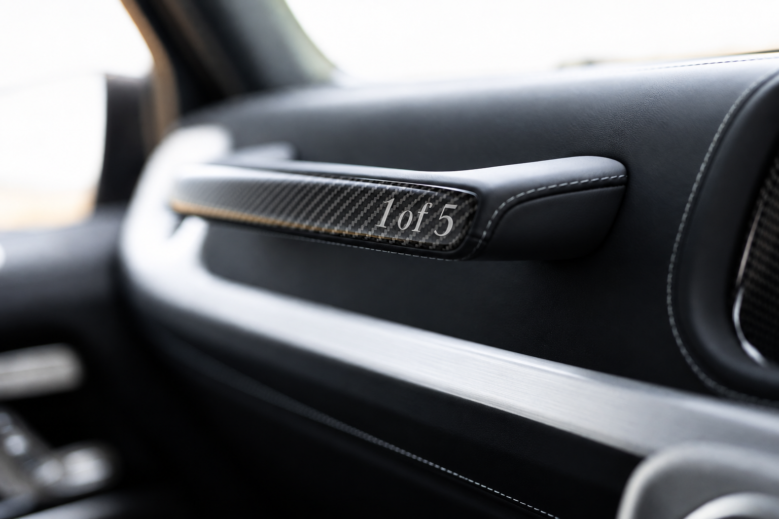Close-up of a car interior door panel with a carbon fiber accent reading '1 of 5', indicating a limited edition or numbered trim piece.