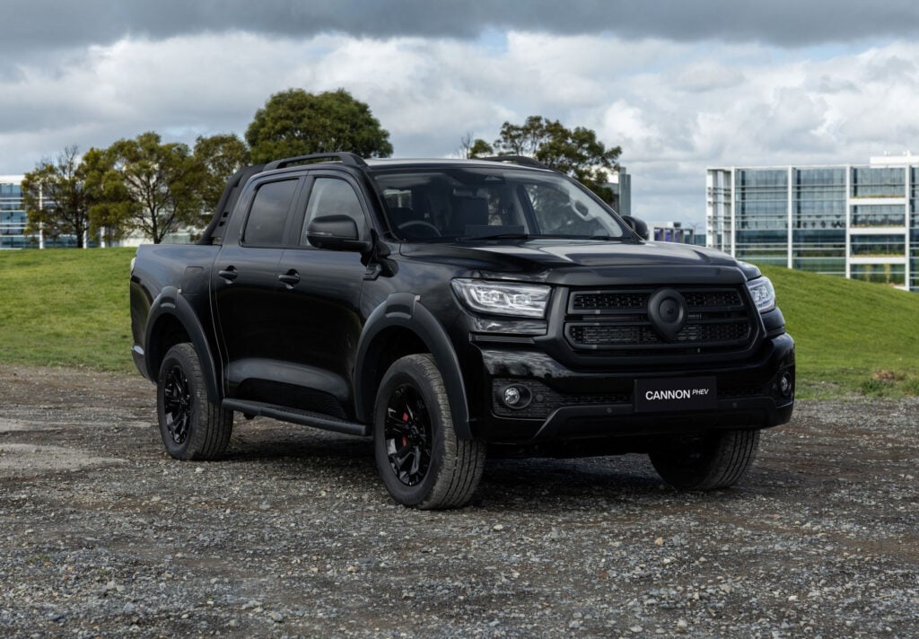 Black pickup truck parked on a gravel lot with modern glass buildings and cloudy sky in the background.
