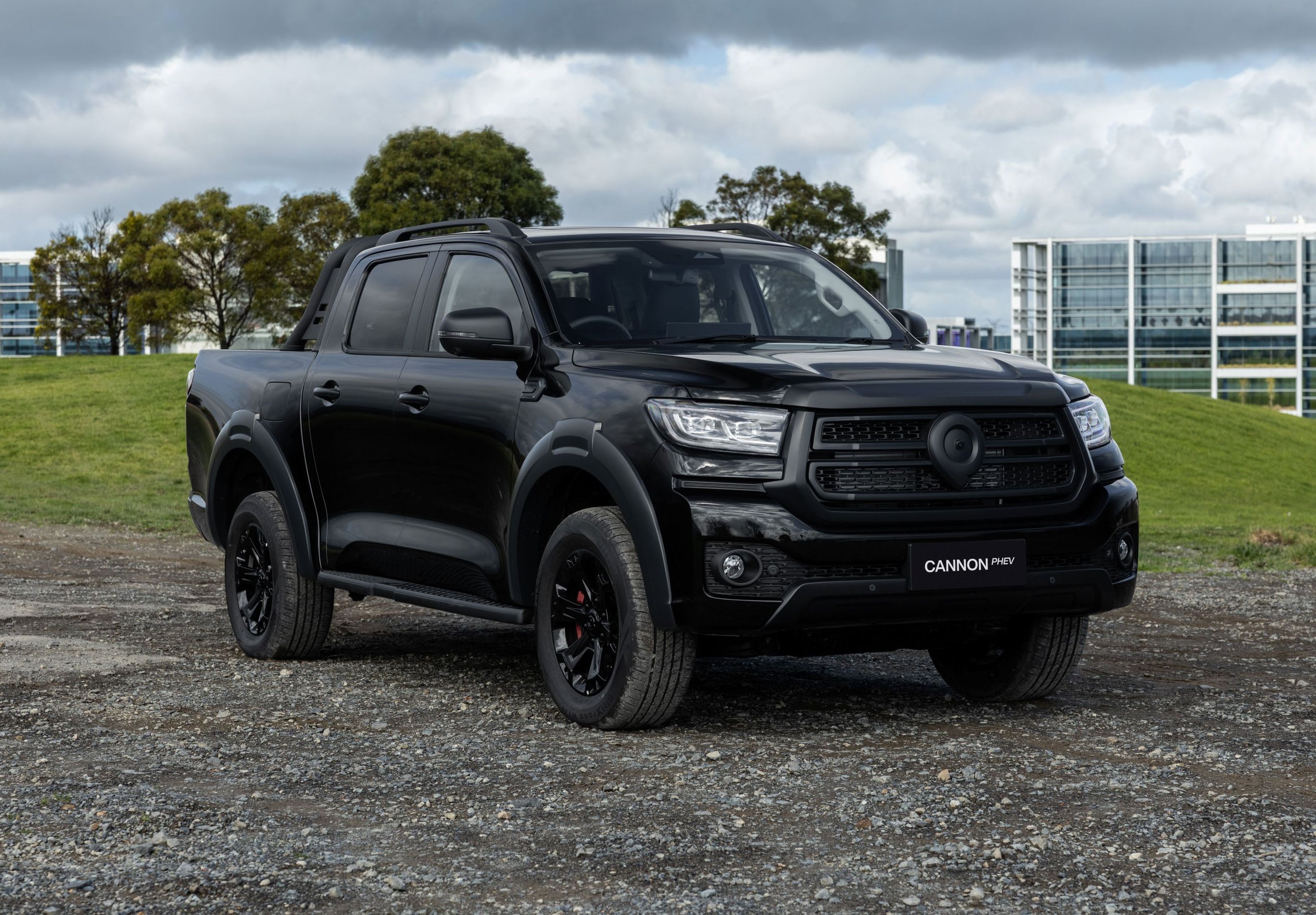 Black pickup truck parked on a gravel lot with modern glass buildings and cloudy sky in the background.