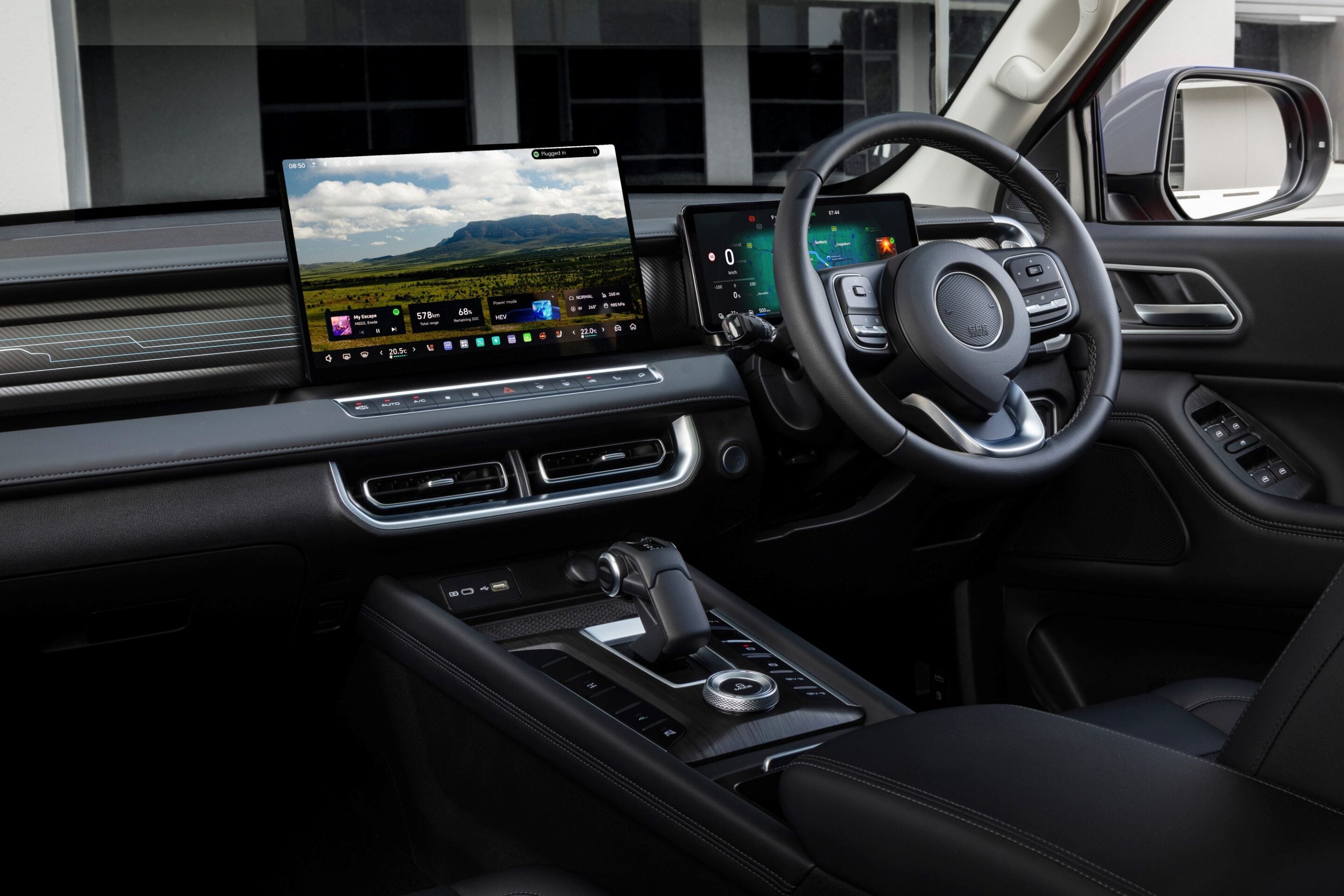 Modern car interior with a wide, curved infotainment screen showing a landscape wallpaper and a second screen near the steering wheel; high-tech dashboard and leather accents