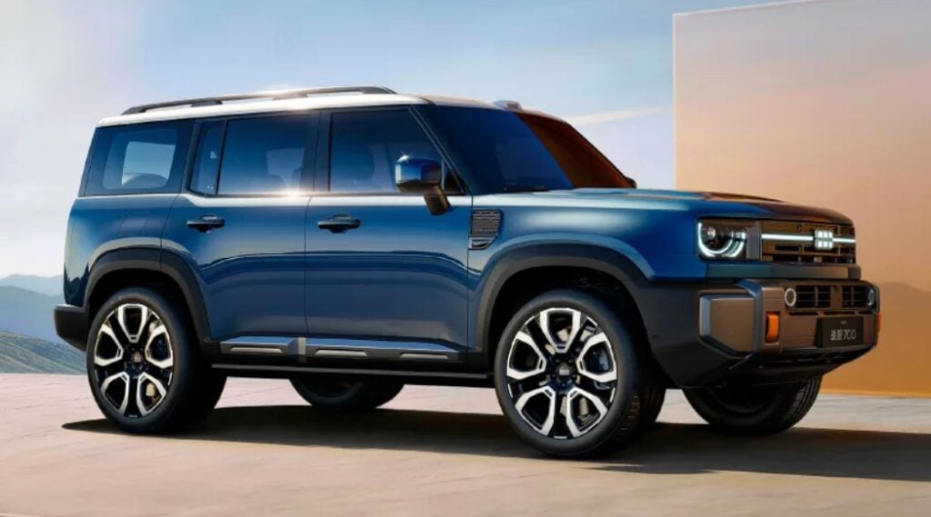 Blue SUV shown in a three-quarter front-view parked on a concrete surface, with mountains in the background and clear sky.
