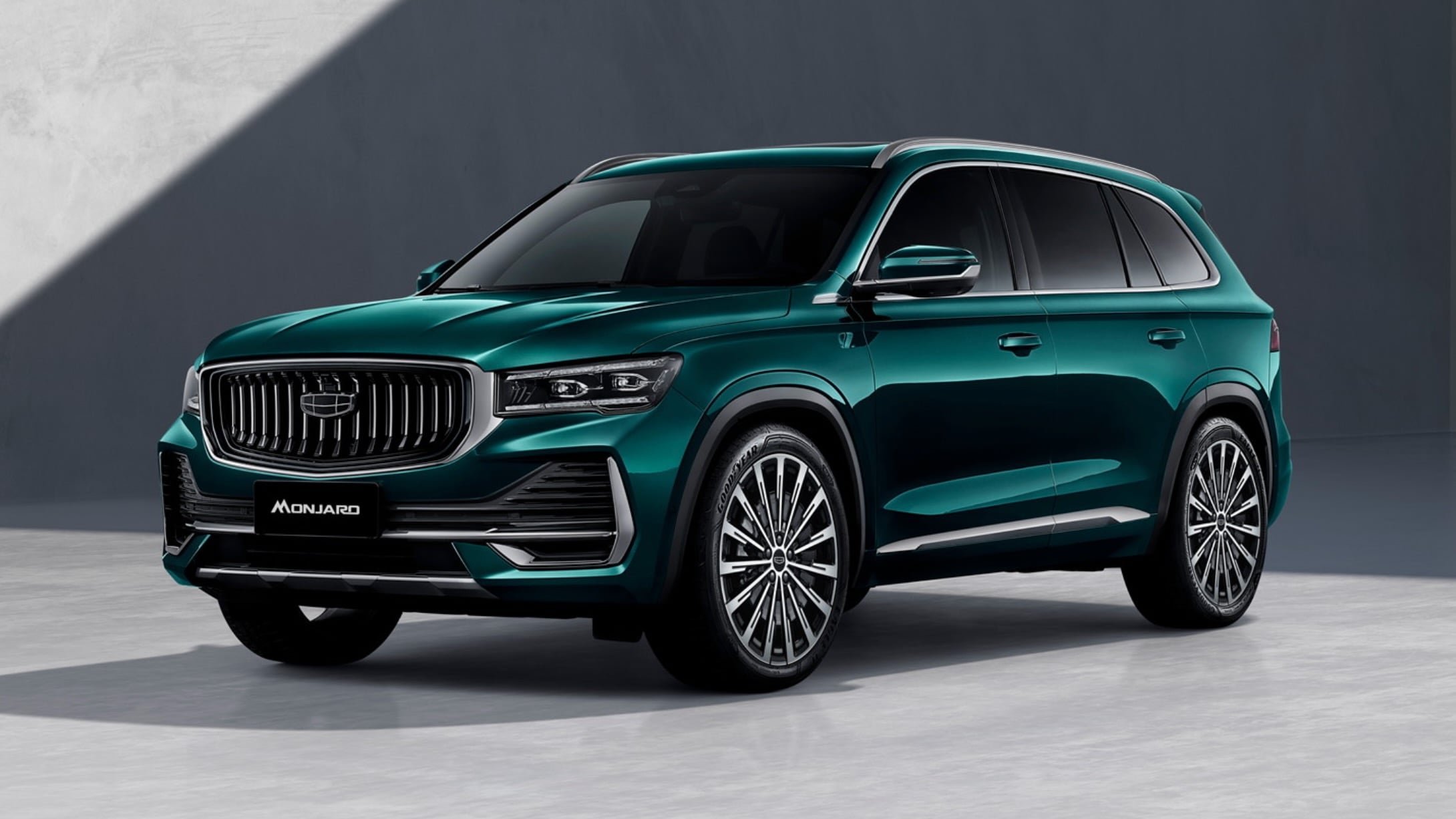 Front three-quarter view of a teal Monjaro SUV in a minimalist indoor setting, showing the bold grille and large alloy wheels.