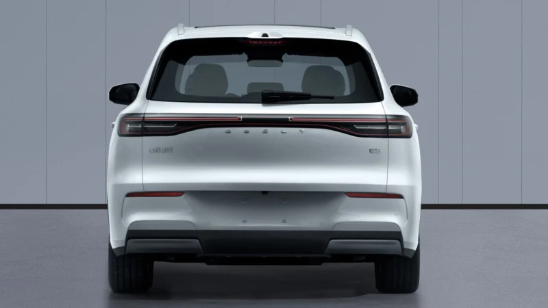 White SUV seen from the rear, parked on a gray surface in front of a gray wall; full-width rear light bar and Porsche badge visible on the tailgate