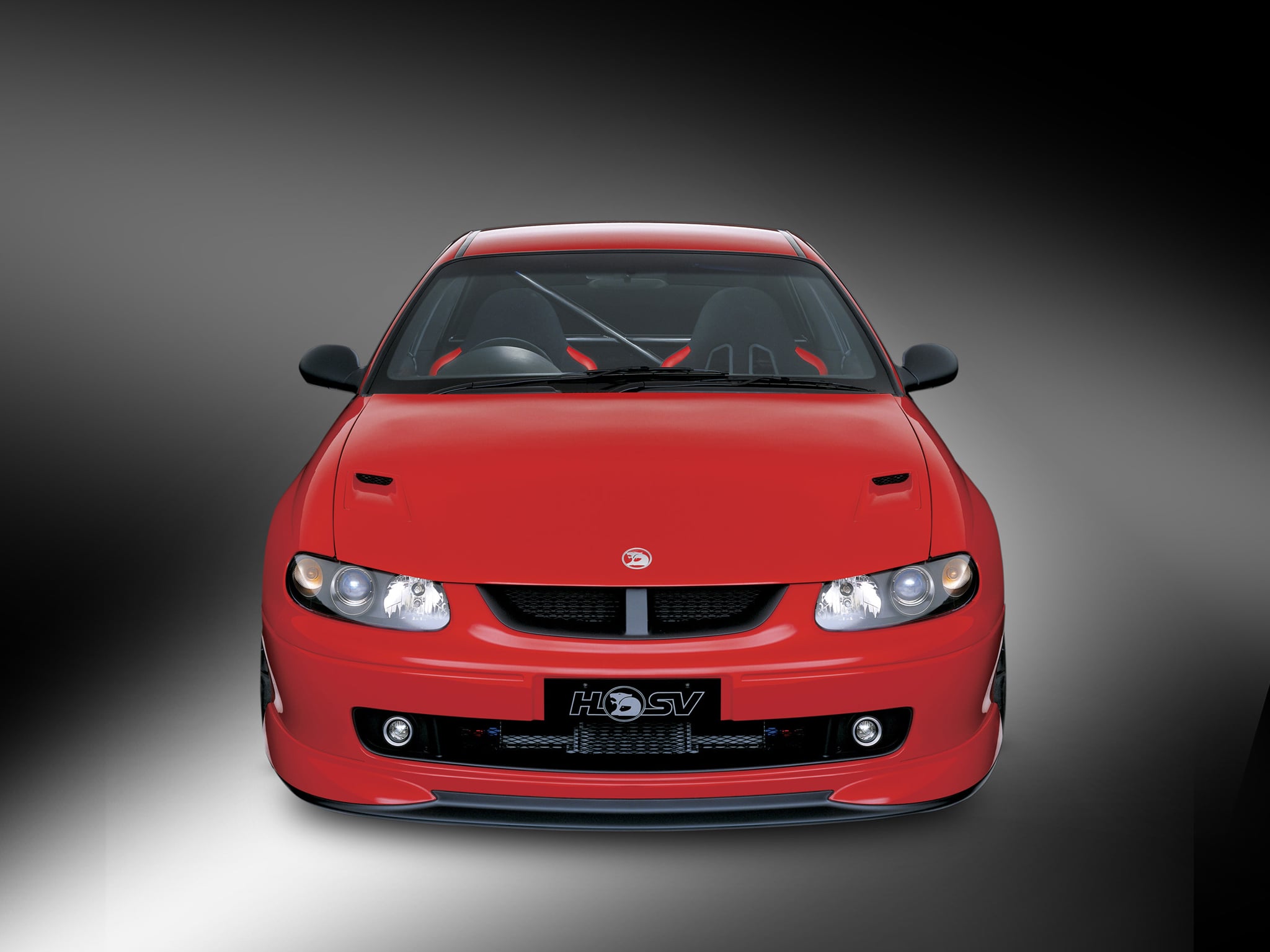 Front view of a red sports car, low angle, headlights and grille visible against a gray gradient background.