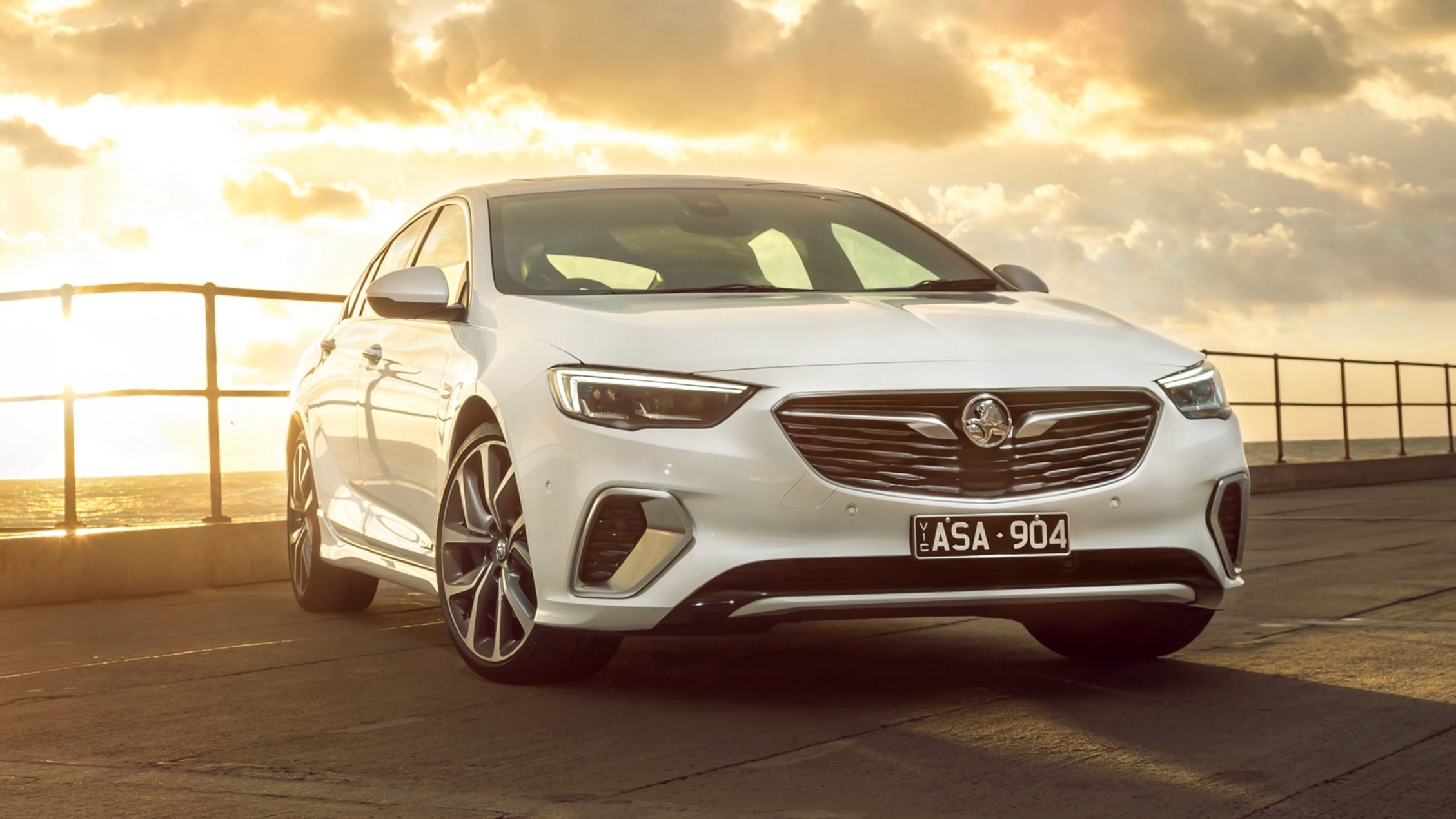 White sedan parked on a waterfront rooftop at sunset, railing in the background and warm golden light.