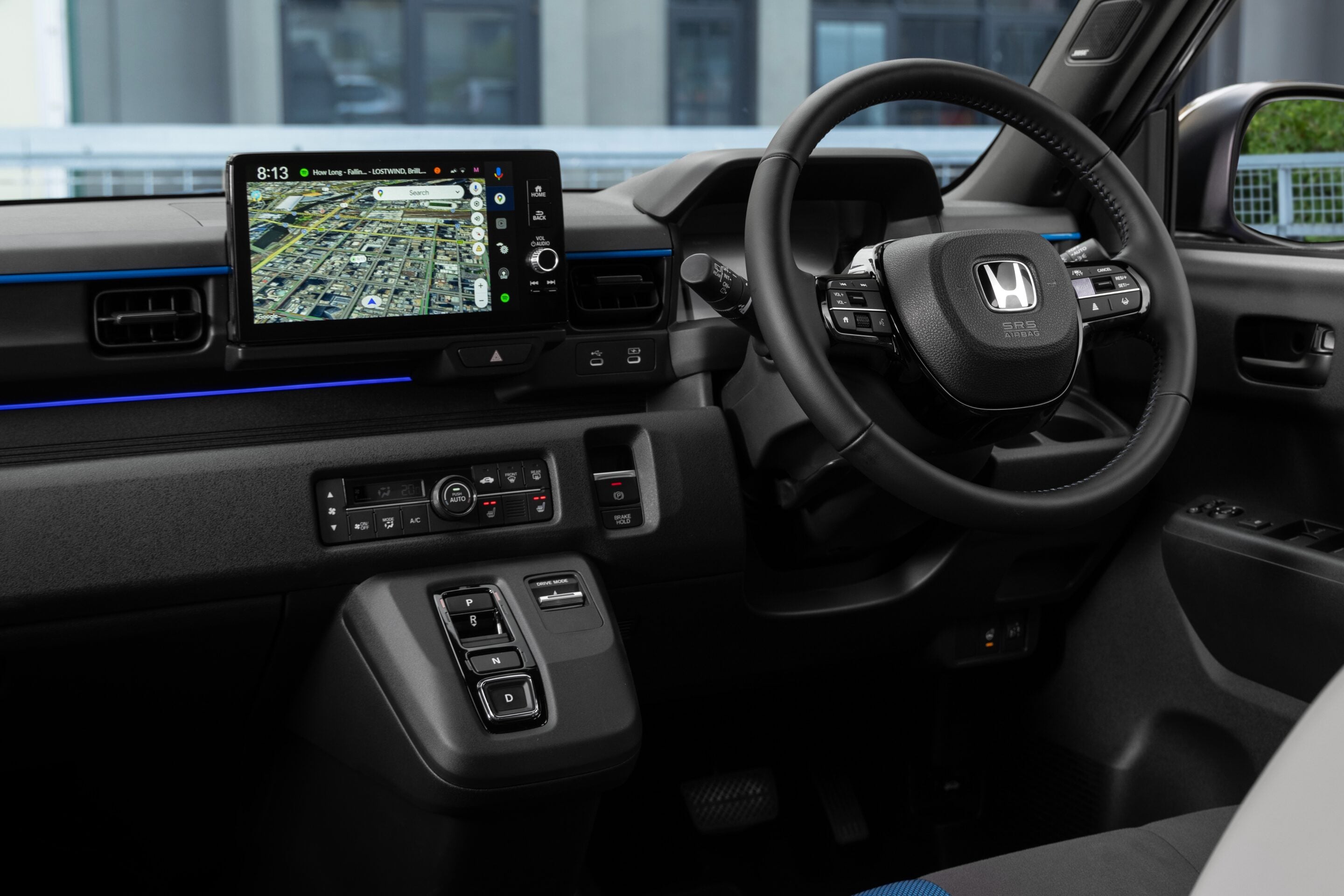 Interior of a modern car cockpit featuring a large central touchscreen, steering wheel with controls, and blue accent lighting.