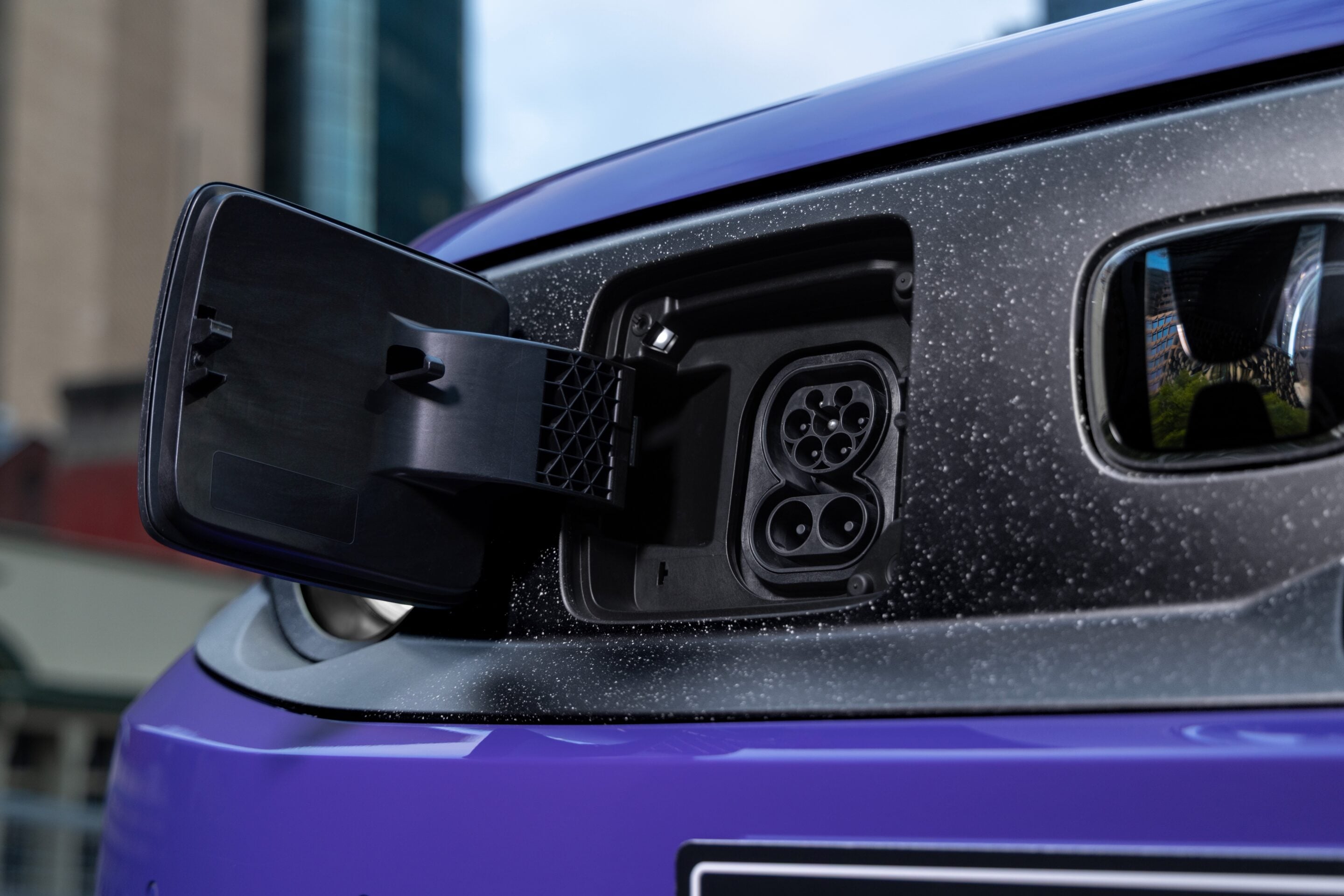 Electric vehicle charging port open on a purple car, showing the multi-pin connector receptacle.