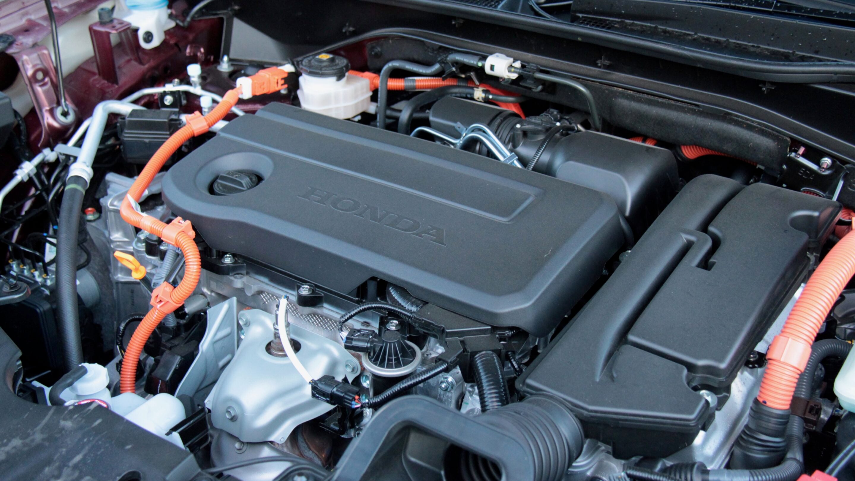 Close-up of a Honda car engine bay with black plastic cover and orange wiring harnesses visible.