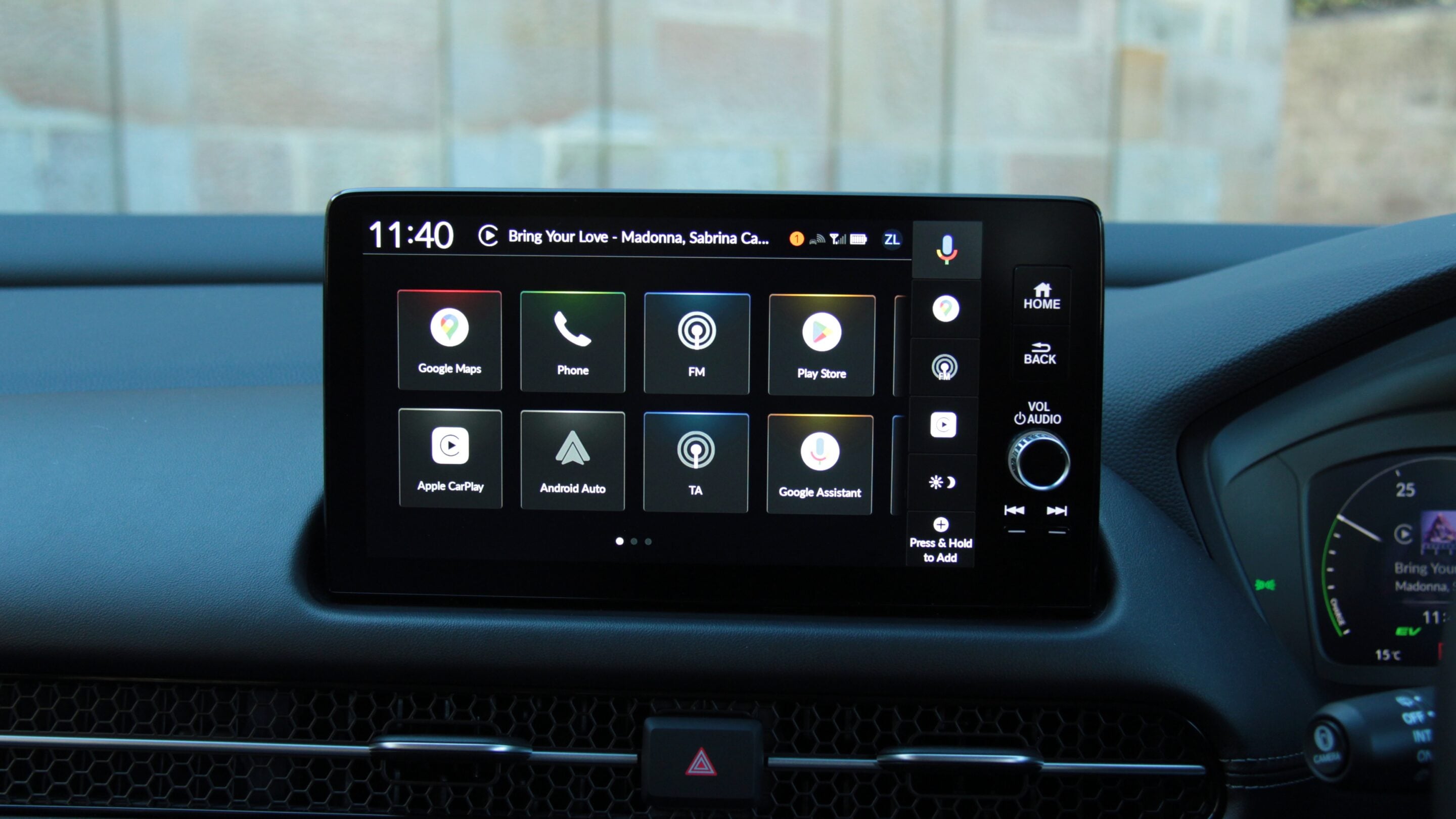 Infotainment touchscreen in a car showing app icons such as Google Maps, Phone, FM, Play Store, Apple CarPlay and Android Auto.