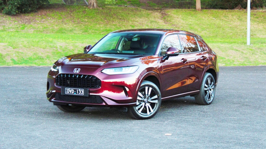 Maroon Honda SUV parked on a paved lot with a grassy embankment in the background.