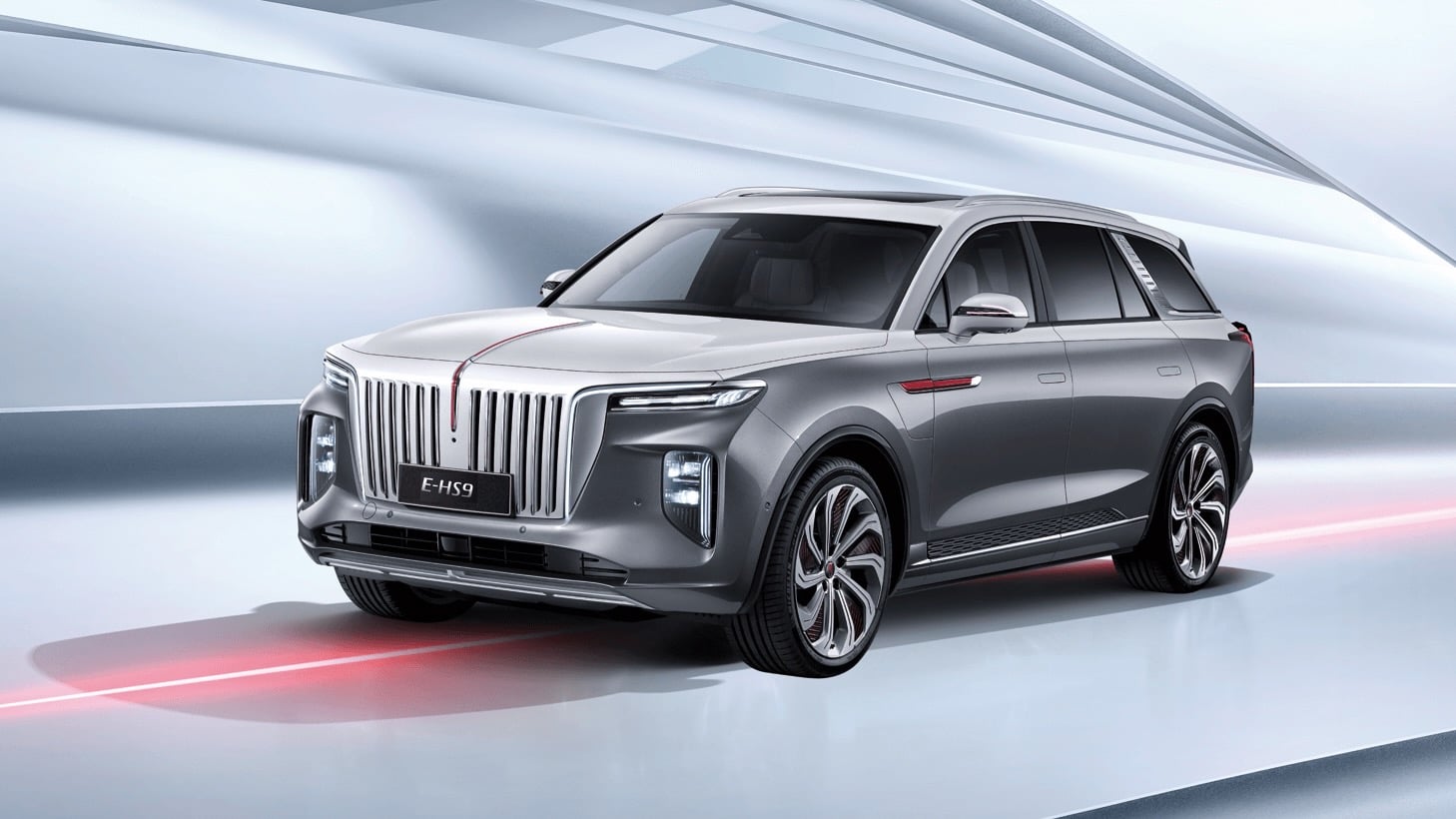 Front three-quarter view of a silver luxury SUV with a bold vertical chrome grille (E-HS9) in a futuristic tunnel setting.