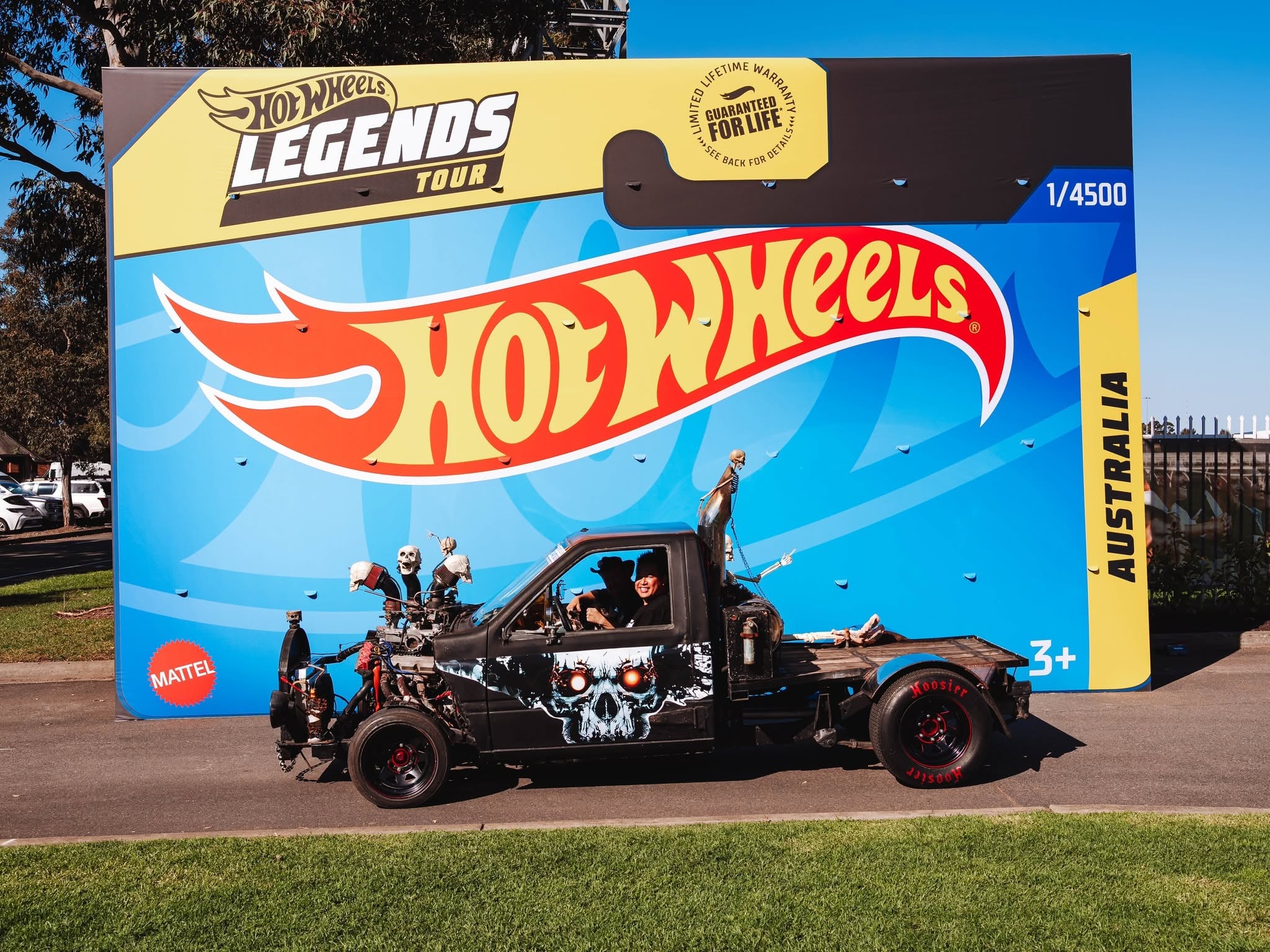 Gigantic Hot Wheels Legends Tour display on a blue mural, featuring a black skull-decorated vehicle in front.