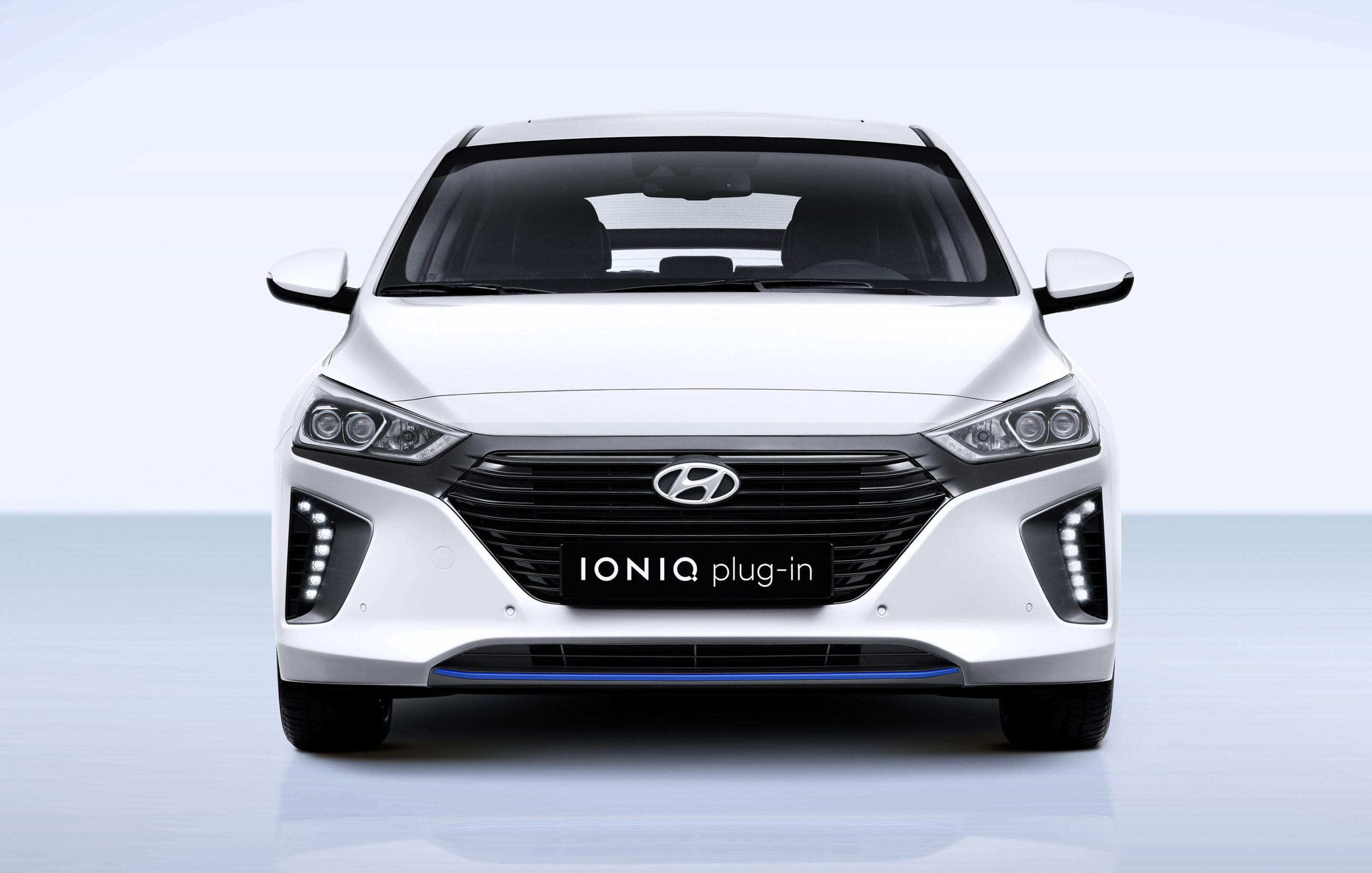 Front view of a white Hyundai IONIQ plug-in car, showing the grille, headlights, and the 'IONIQ plug-in' plate text.