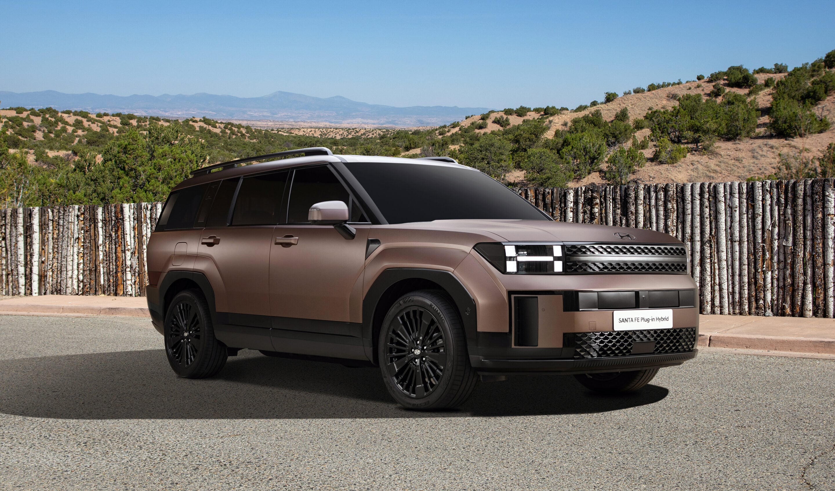 Bronze Hyundai Santa Fe Plug-in Hybrid SUV parked by a wooden fence with desert hills and blue sky in the background.