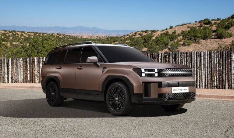 Bronze Hyundai Santa Fe Plug-in Hybrid SUV parked by a wooden fence with desert hills and blue sky in the background.