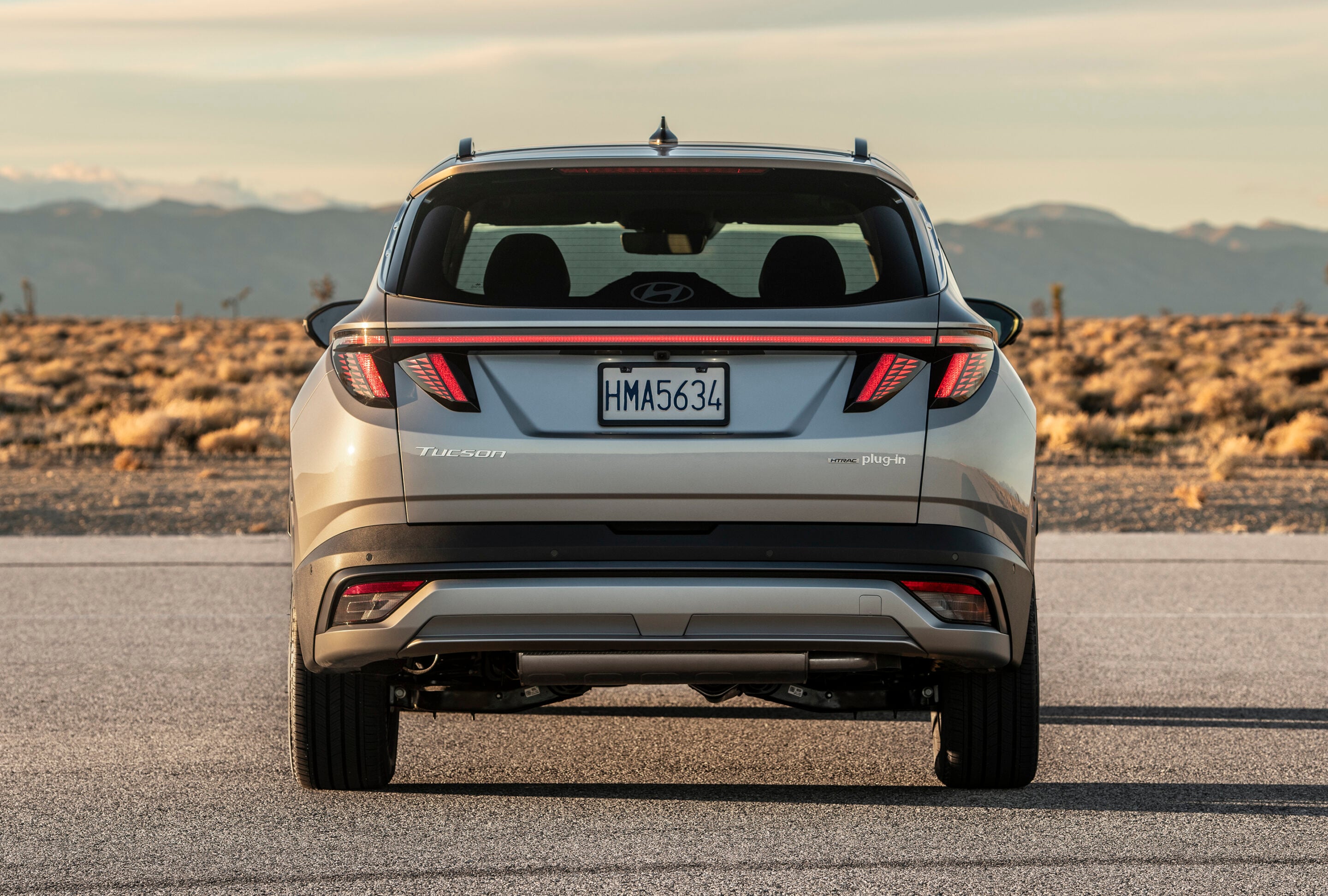 Rear view of a silver Hyundai Tucson on a desert road at sunset, license plate HMA5634.