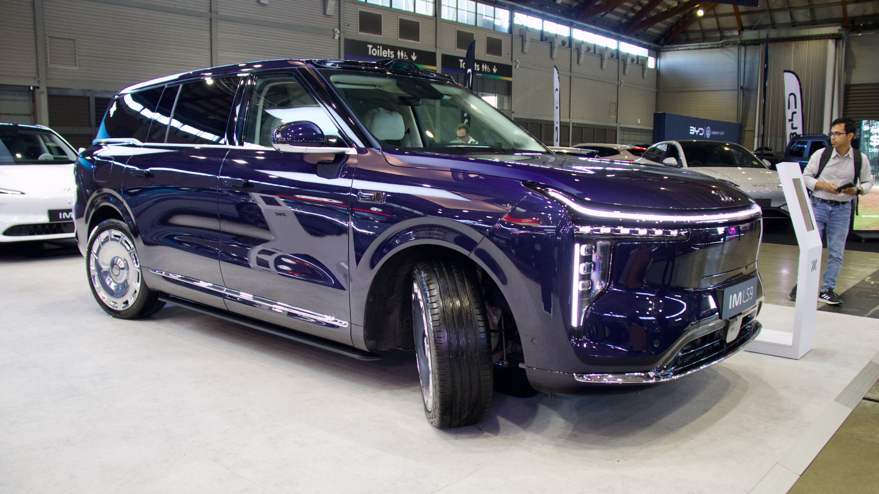 Dark blue luxury SUV on display at an auto show with chrome trim and a prominent grille nearby.