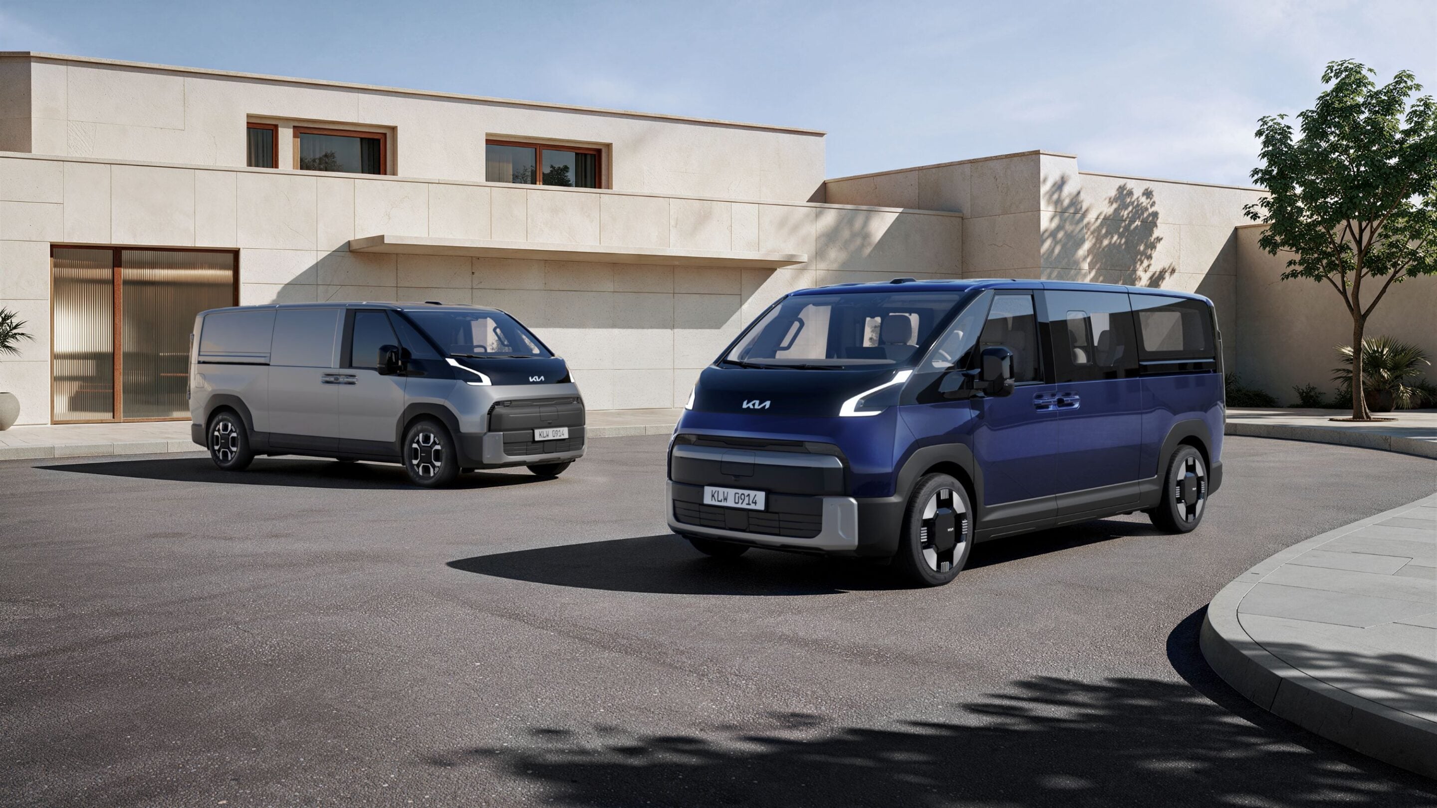 Two modern vans parked in a driveway in front of a beige building, with one blue van in the foreground and a gray van behind.