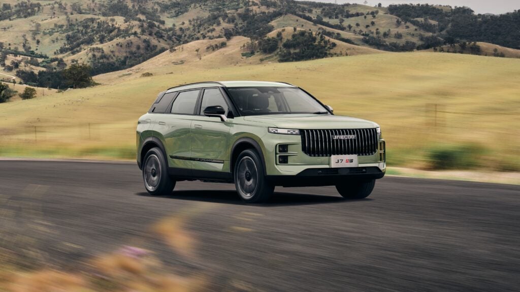 Green SUV driving along a rural road with rolling hills in the background.