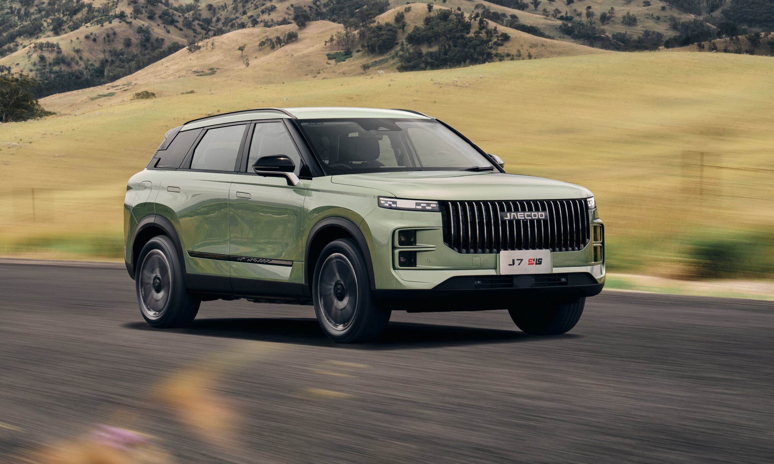 Green SUV in motion on a rural road with golden hills in the background.