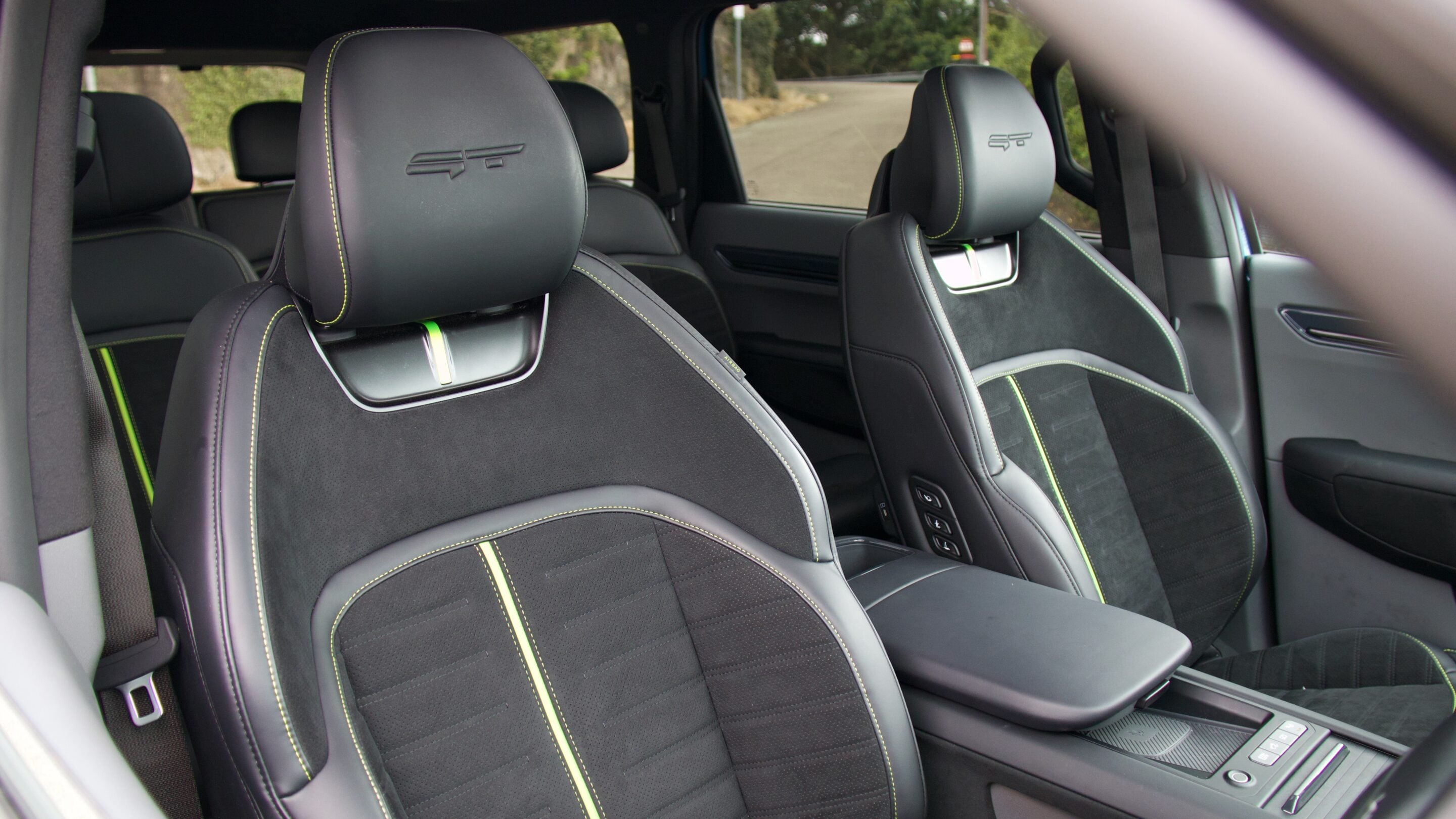 Front seats in a black leather car interior with lime-green stitching and headrest embroidery.