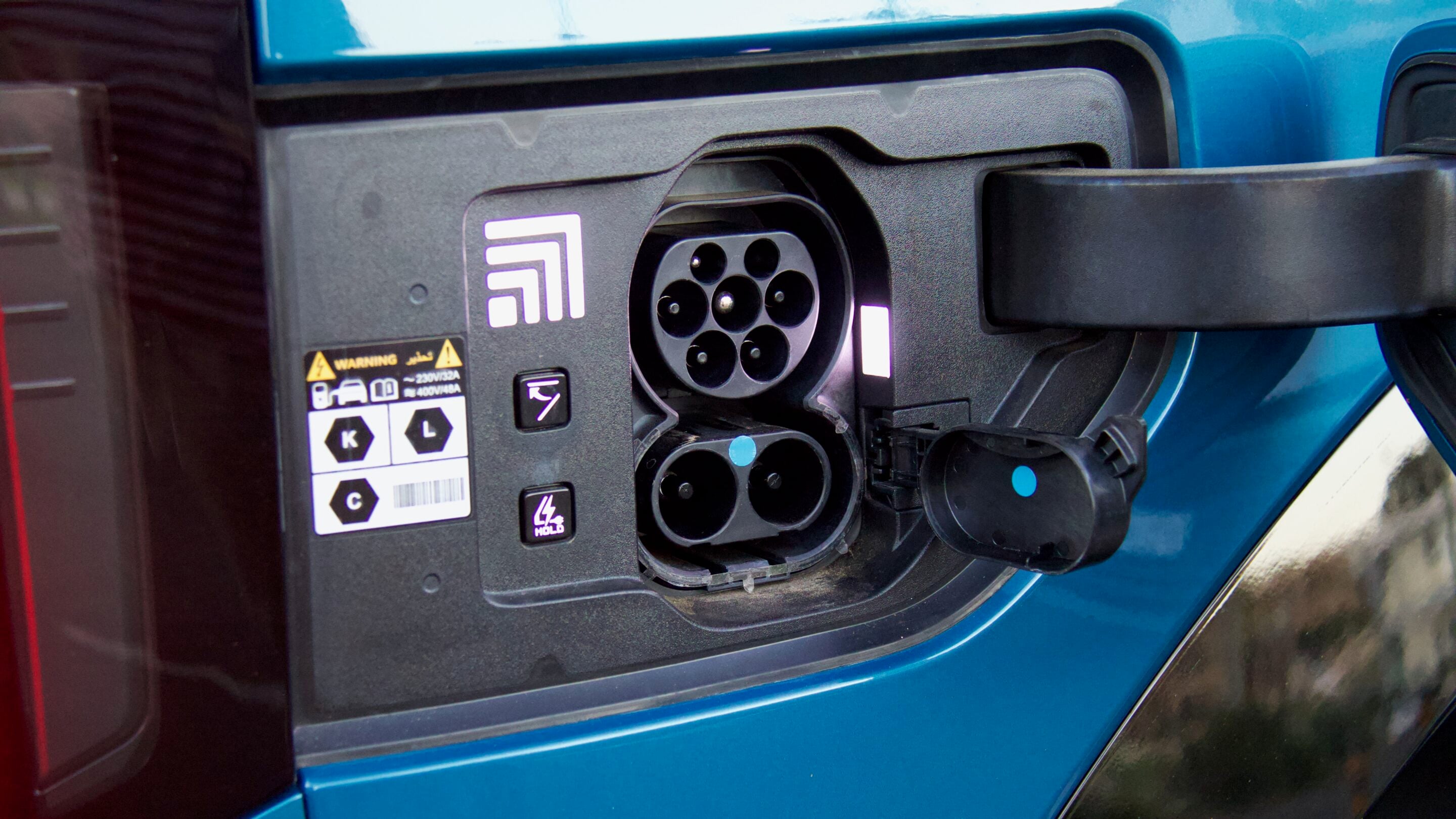 Close-up of an electric vehicle charging inlet with multiple circular sockets on a blue car.