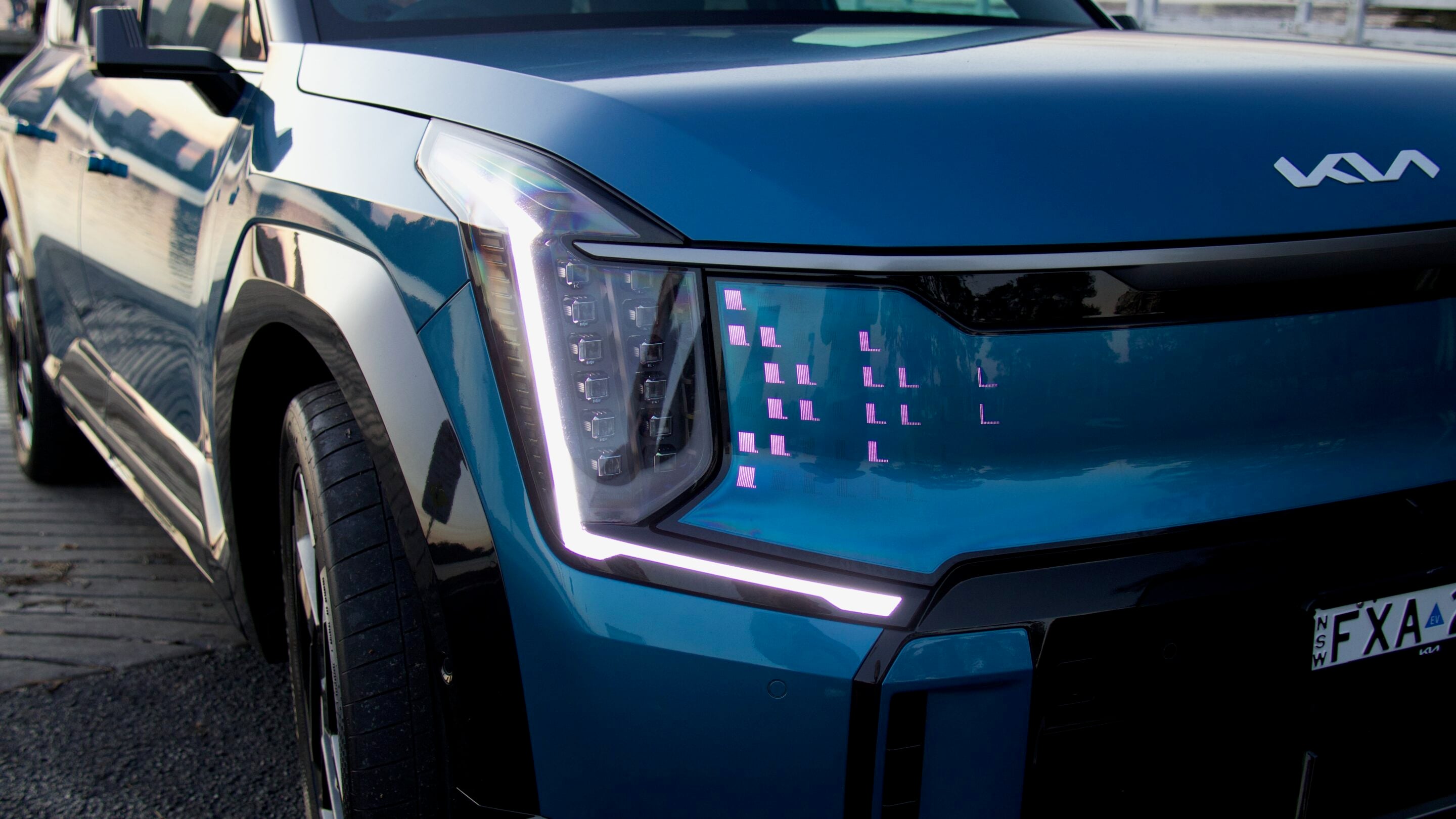 Close-up of the front left side of a blue SUV, showing a tall vertical LED headlight and glossy hood details.