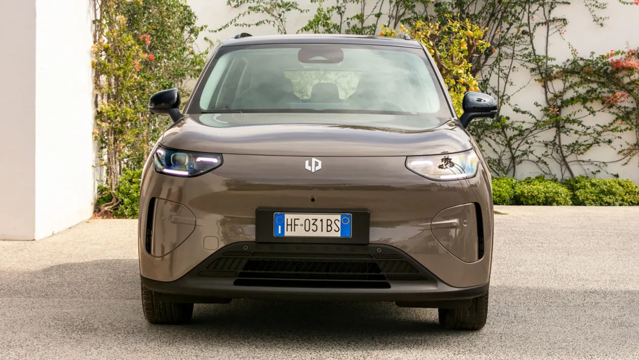 Front view of a brown compact car with European plate HF-031BS on a driveway, greenery in the background.