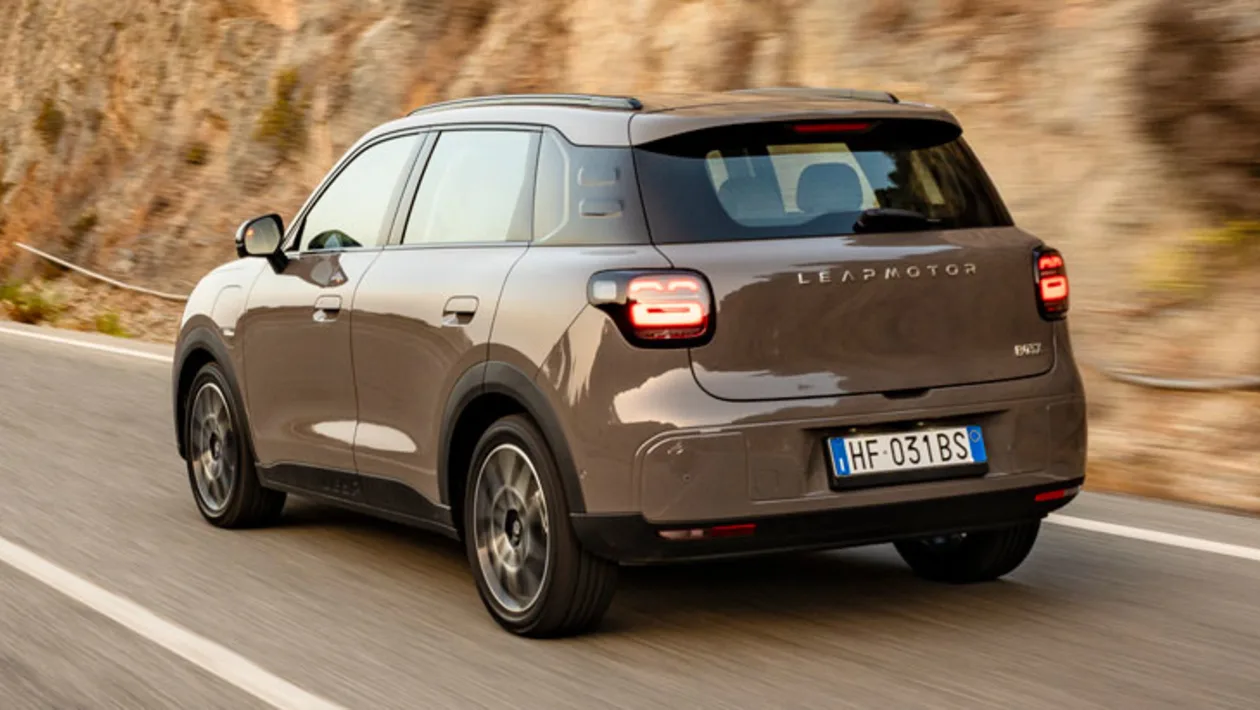 Rear view of a gray Leapmotor SUV driving on a winding mountain road; the car's taillights are on and the European license plate is visible.