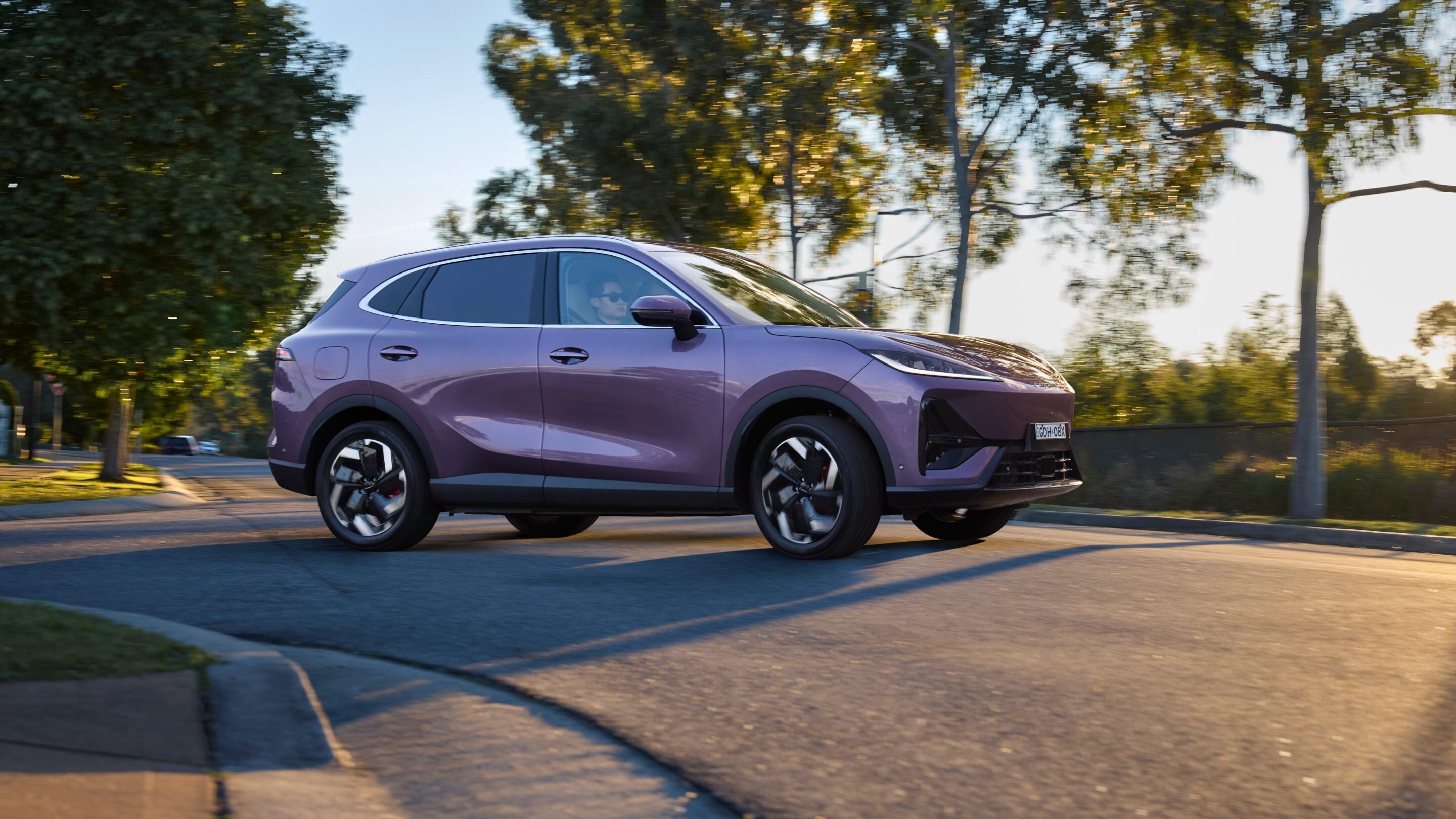 Purple SUV driving on a tree-lined suburban street at sunset.